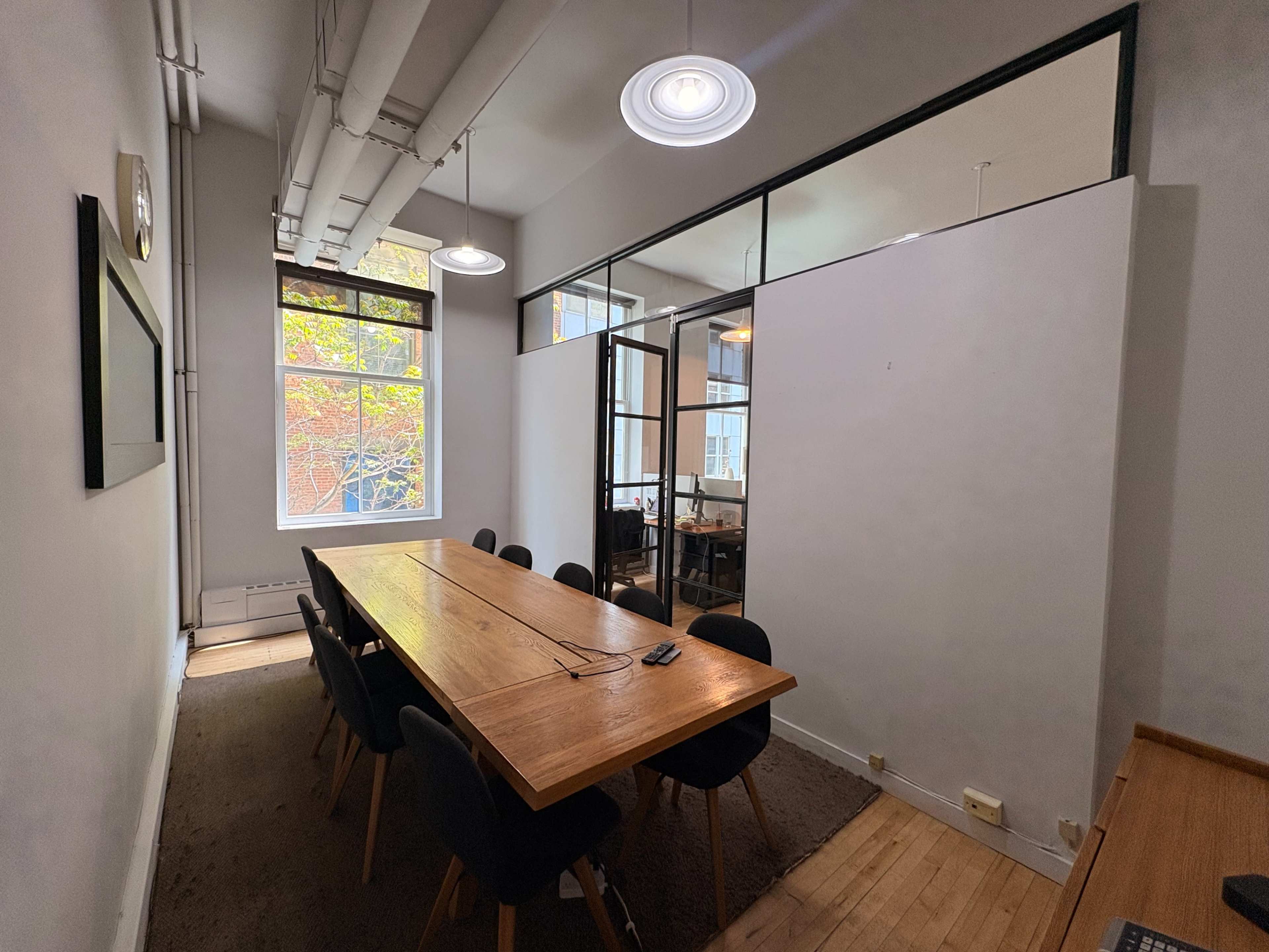The image shows a modern conference room with a long wooden table surrounded by black chairs, and large windows providing natural light.