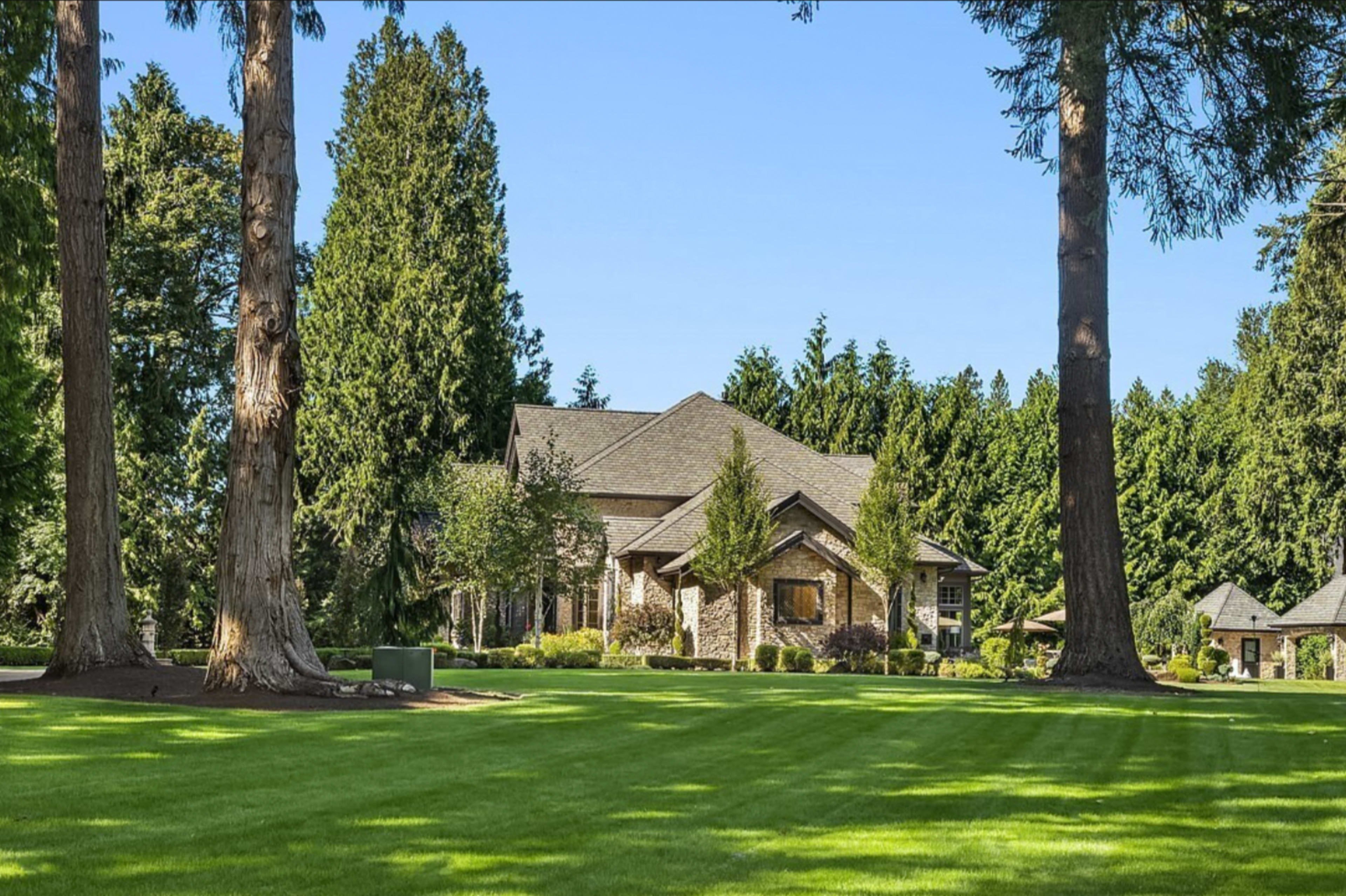 A large, stone house is situated amidst tall trees on a well-maintained lawn.