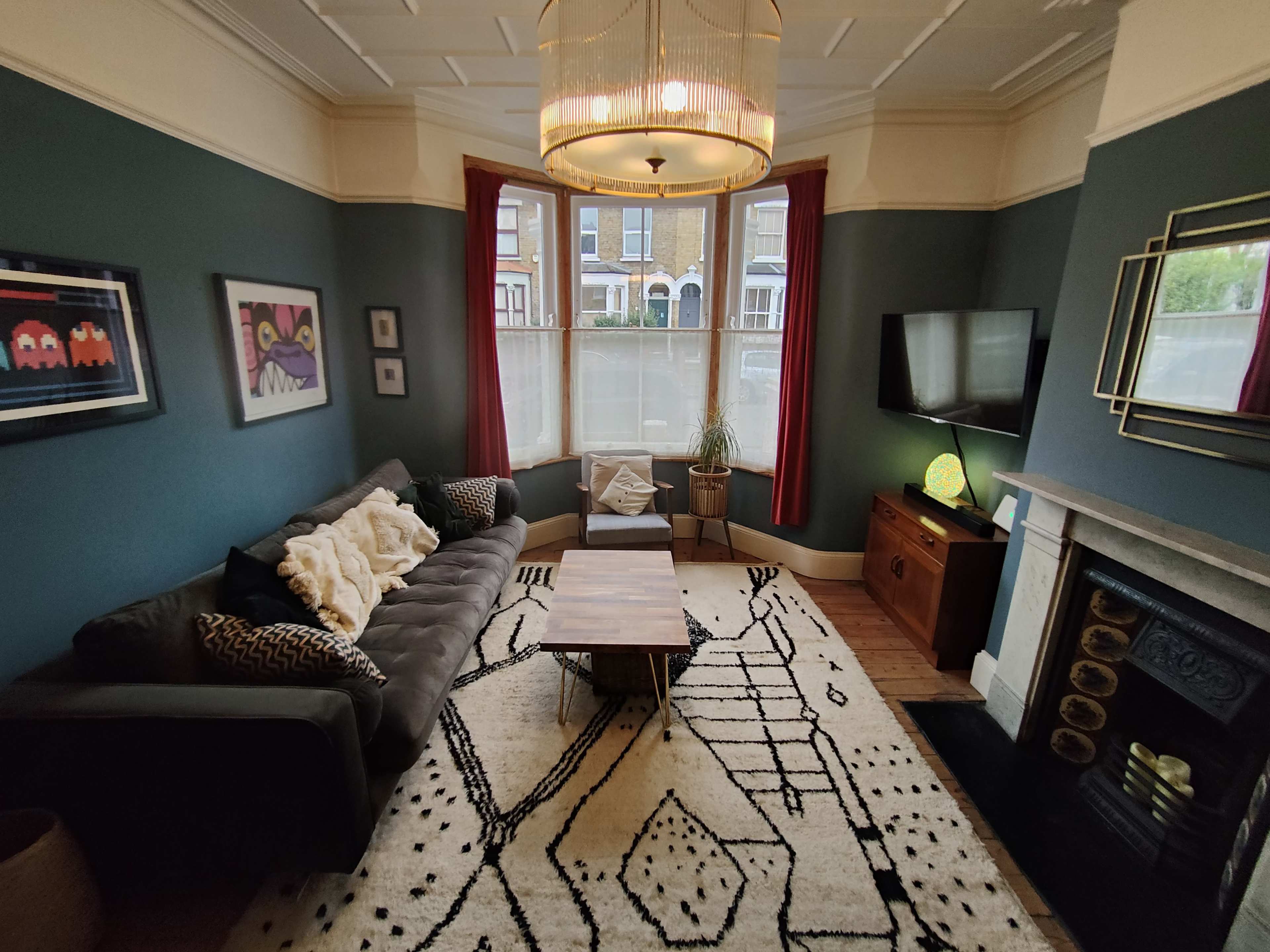 The living room features a dark gray sectional sofa, a coffee table on a patterned rug, and a large window with sheer curtains.