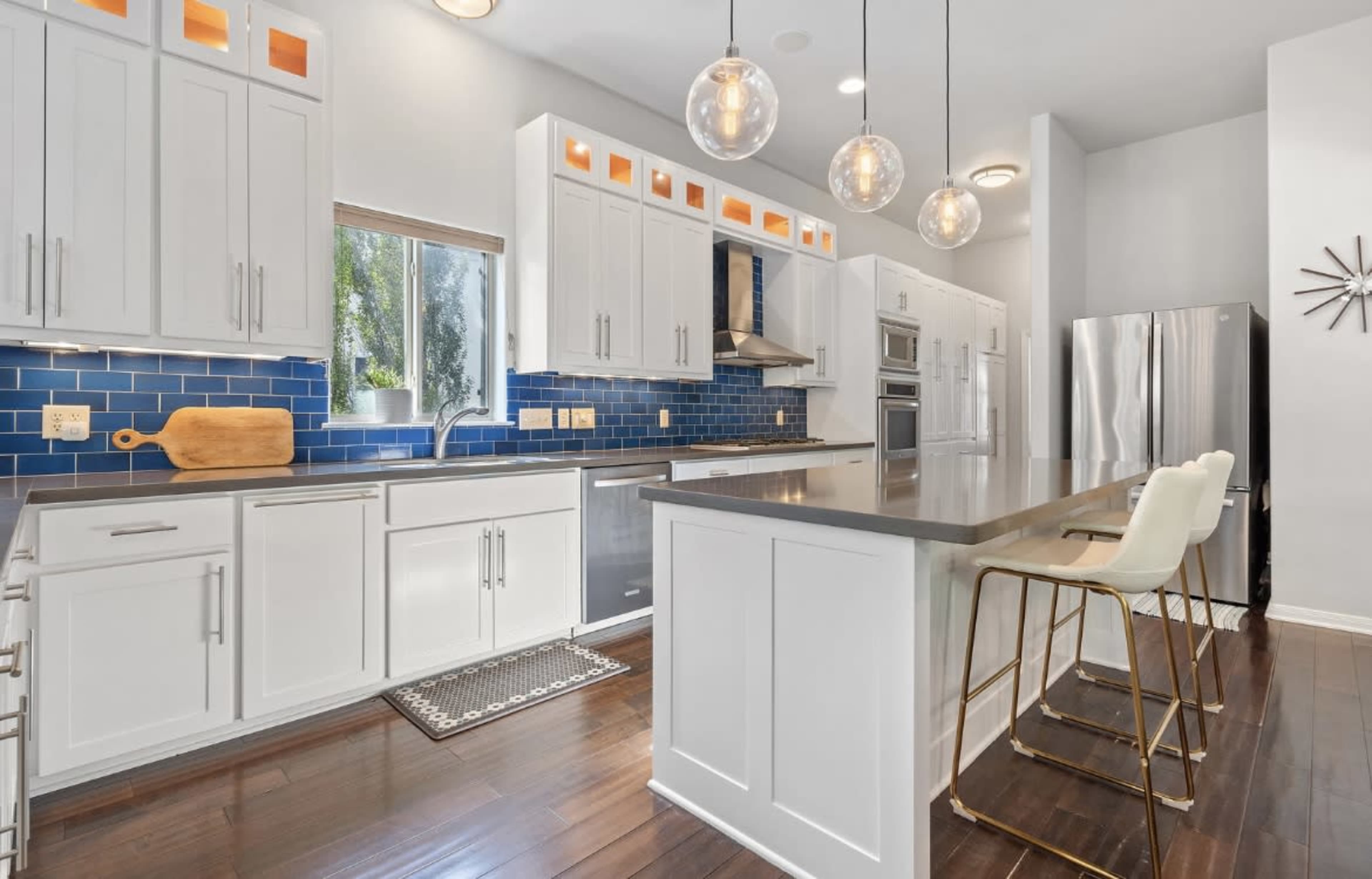 A modern kitchen featuring white cabinets, blue tile backsplash, stainless steel appliances, and a large island with seating.