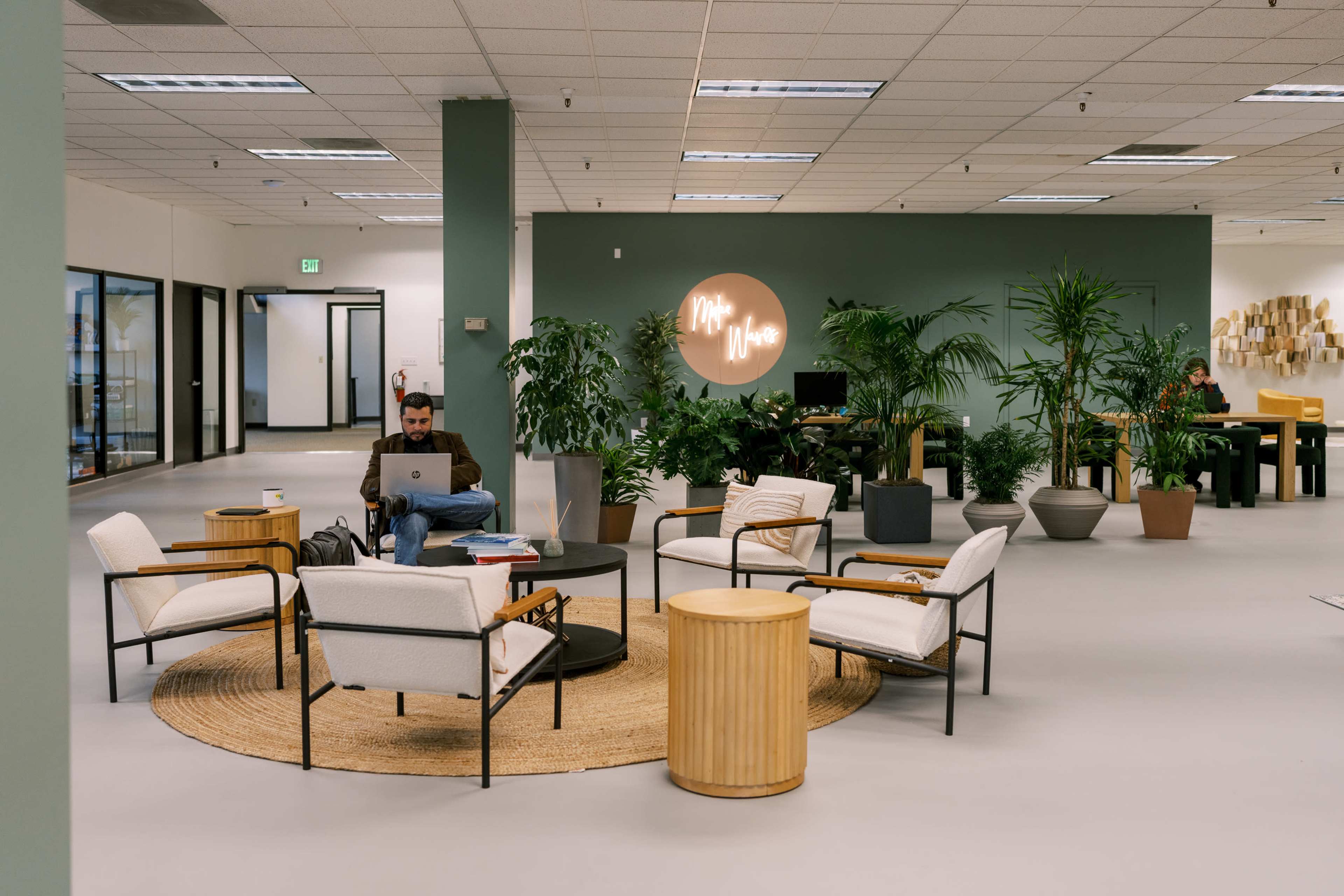 A man works on his laptop in a modern, well-lit office space surrounded by plants and comfortable seating.