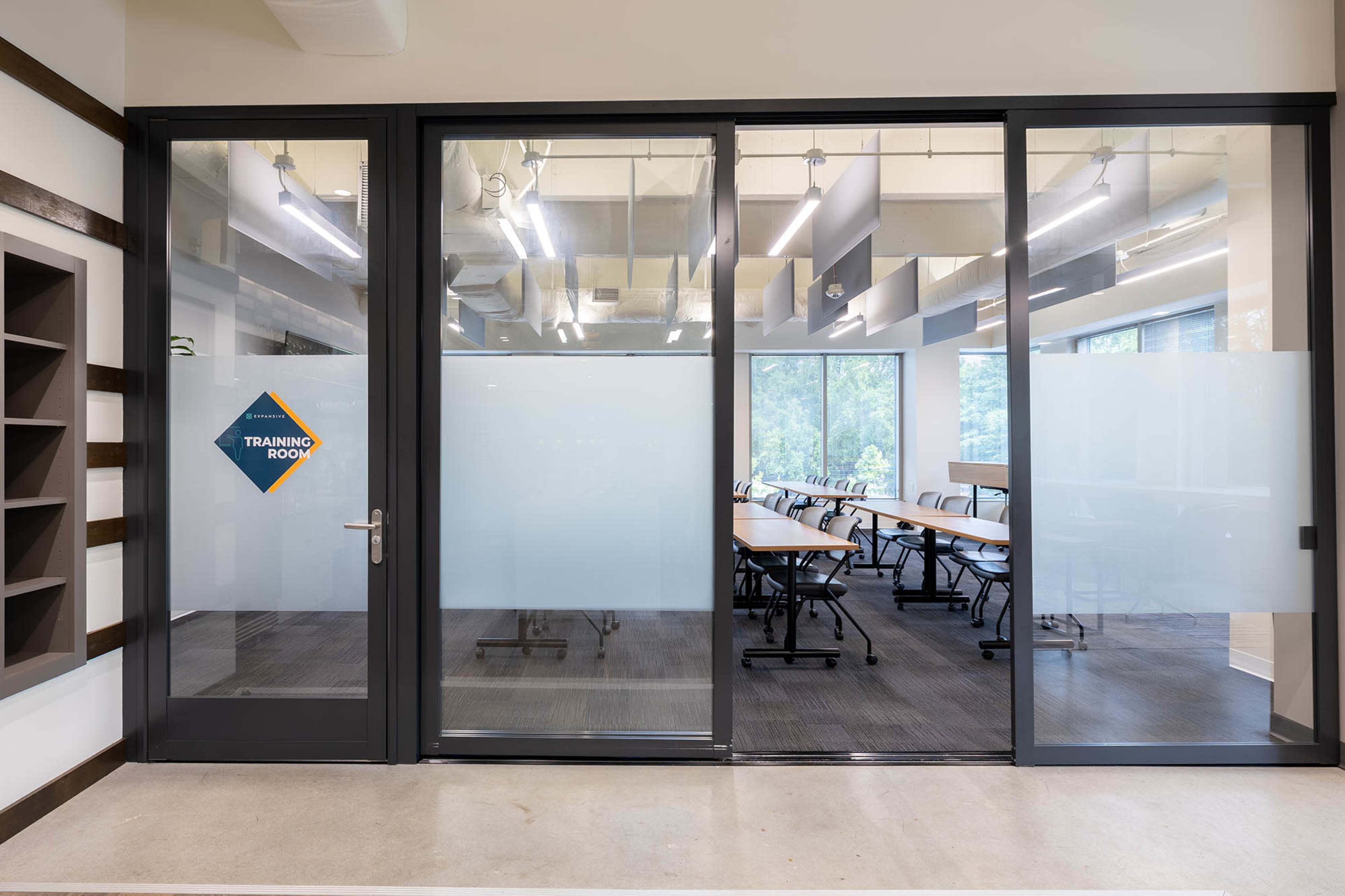 The image shows the entrance to a training room with glass doors, featuring a sign and rows of chairs and tables visible inside.