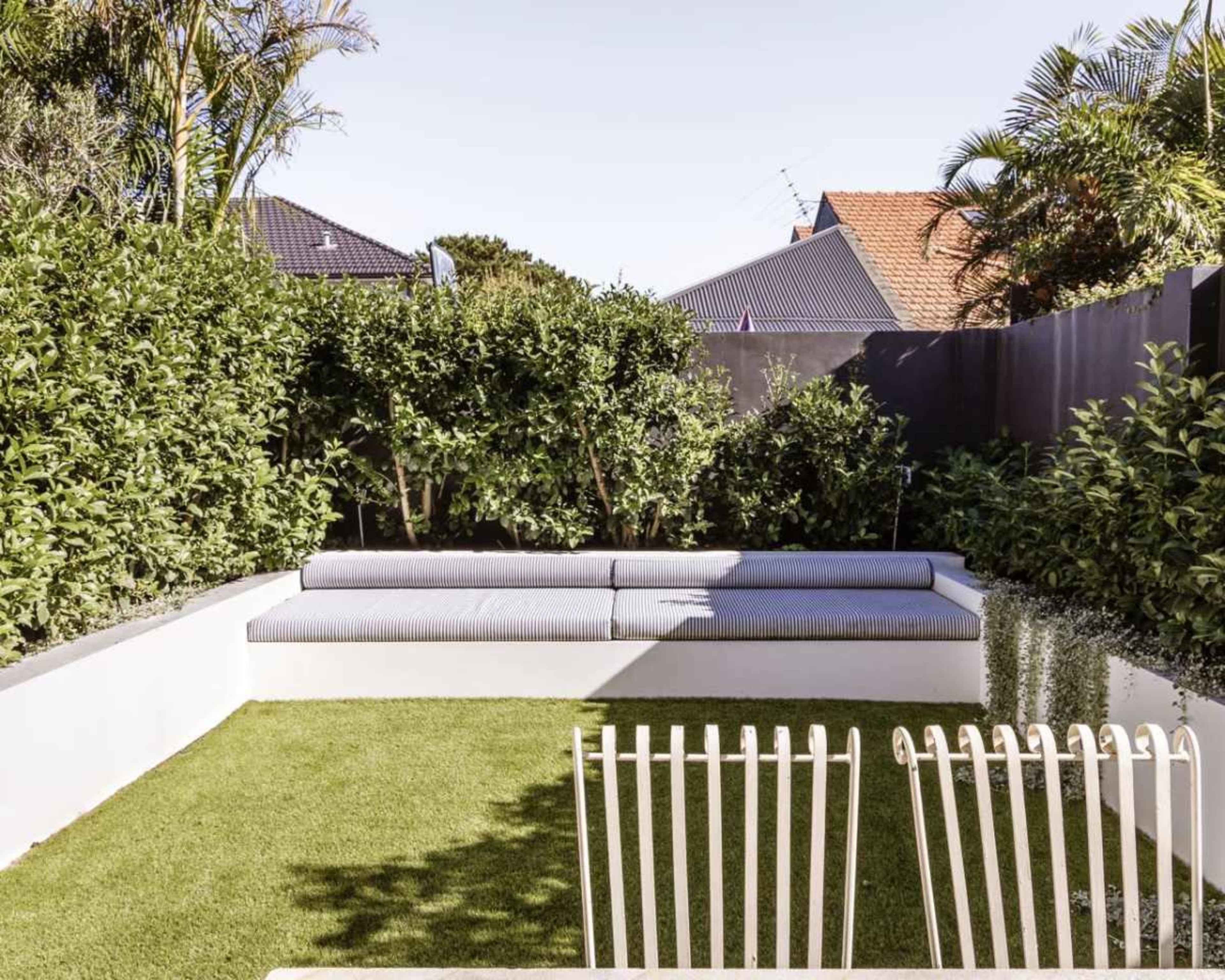 The image shows a neatly landscaped backyard featuring a green lawn, a built-in bench with cushions, and surrounding shrubs.