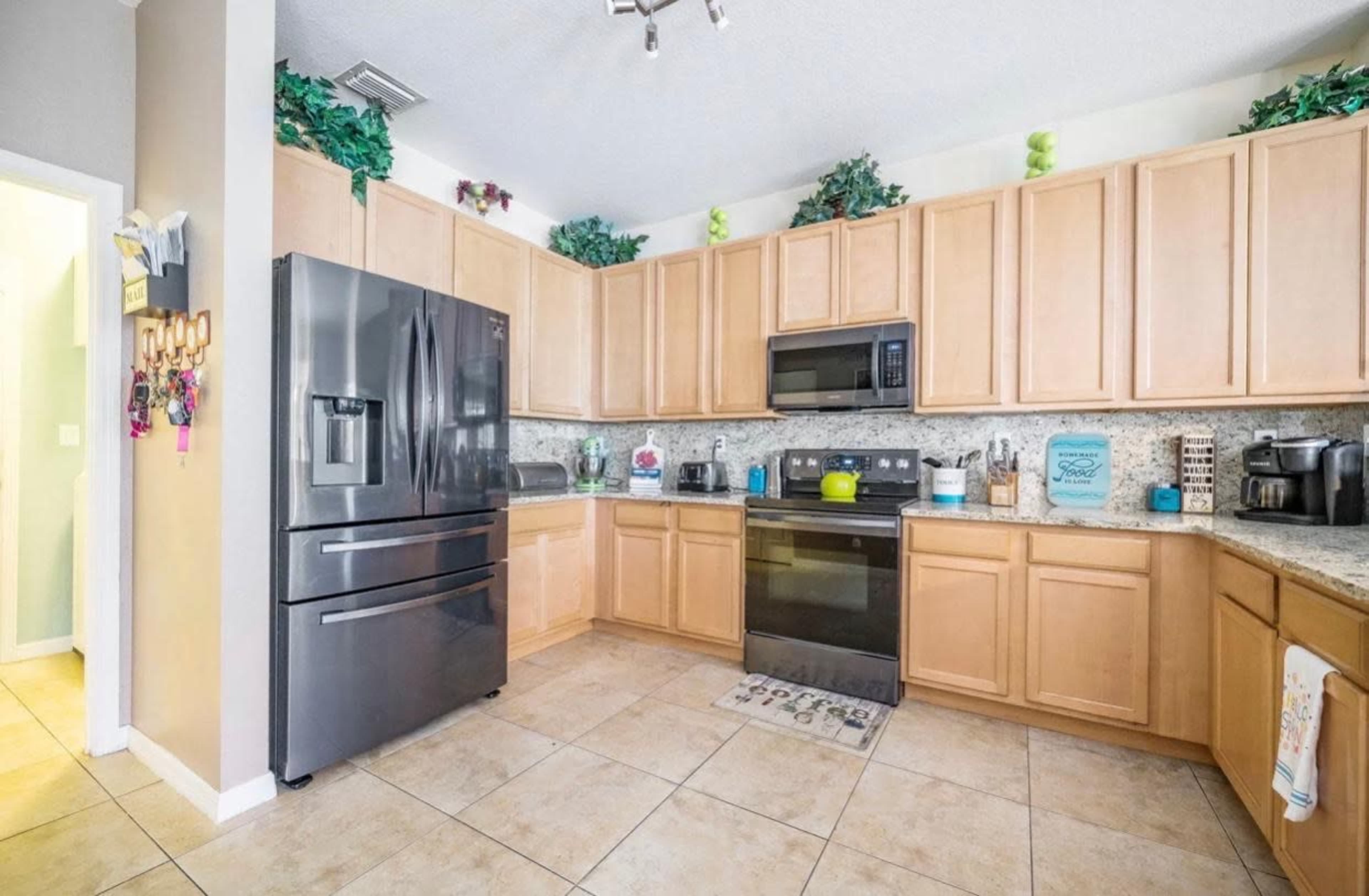A kitchen with wooden cabinets, black appliances, and a tiled floor, featuring organized countertops and decorative plants.