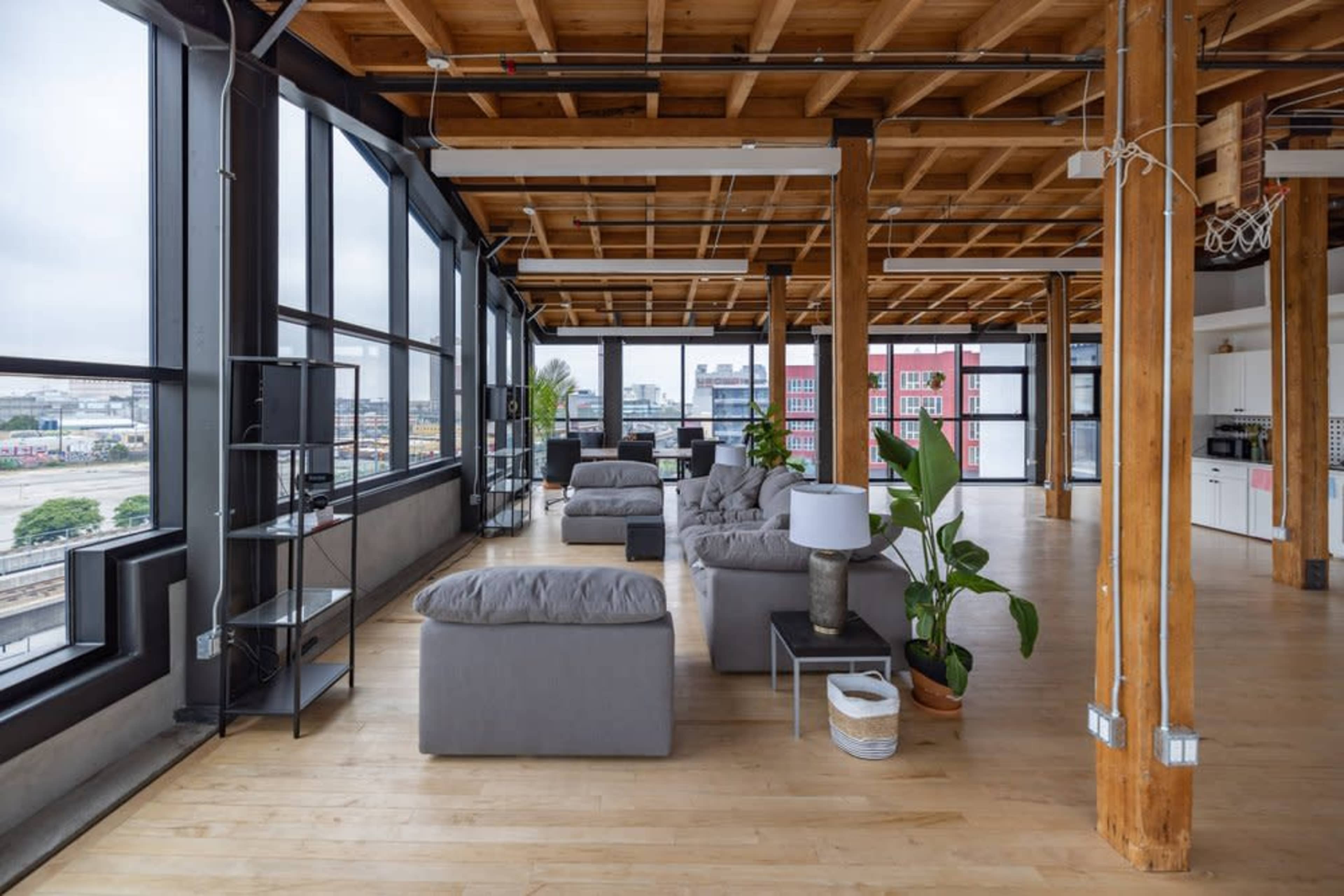 A spacious, modern loft interior with large windows, wooden beams, and gray furniture.