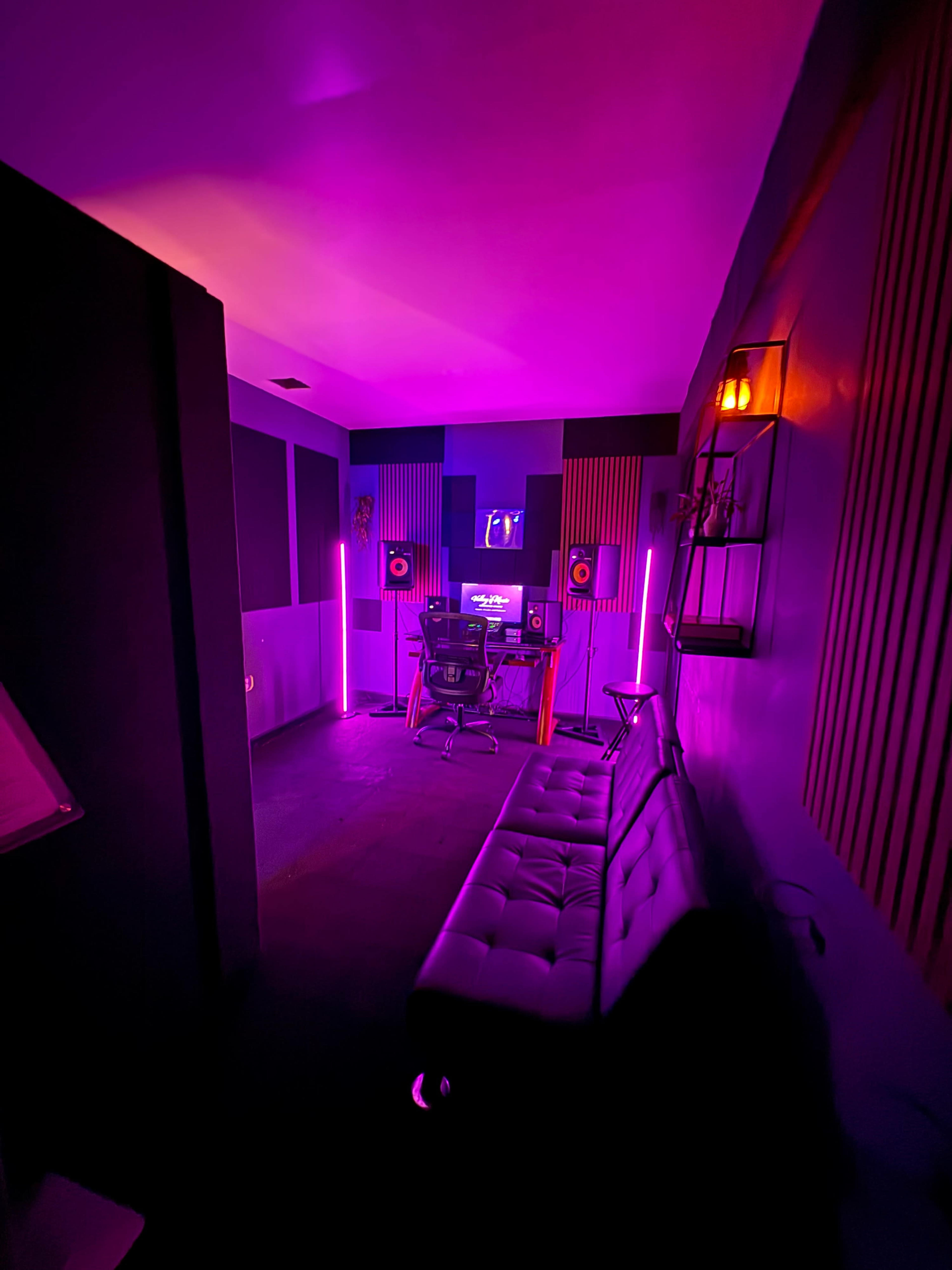 The image shows a dimly lit music studio featuring a desk with speakers, a chair, and purple neon lights along the walls.