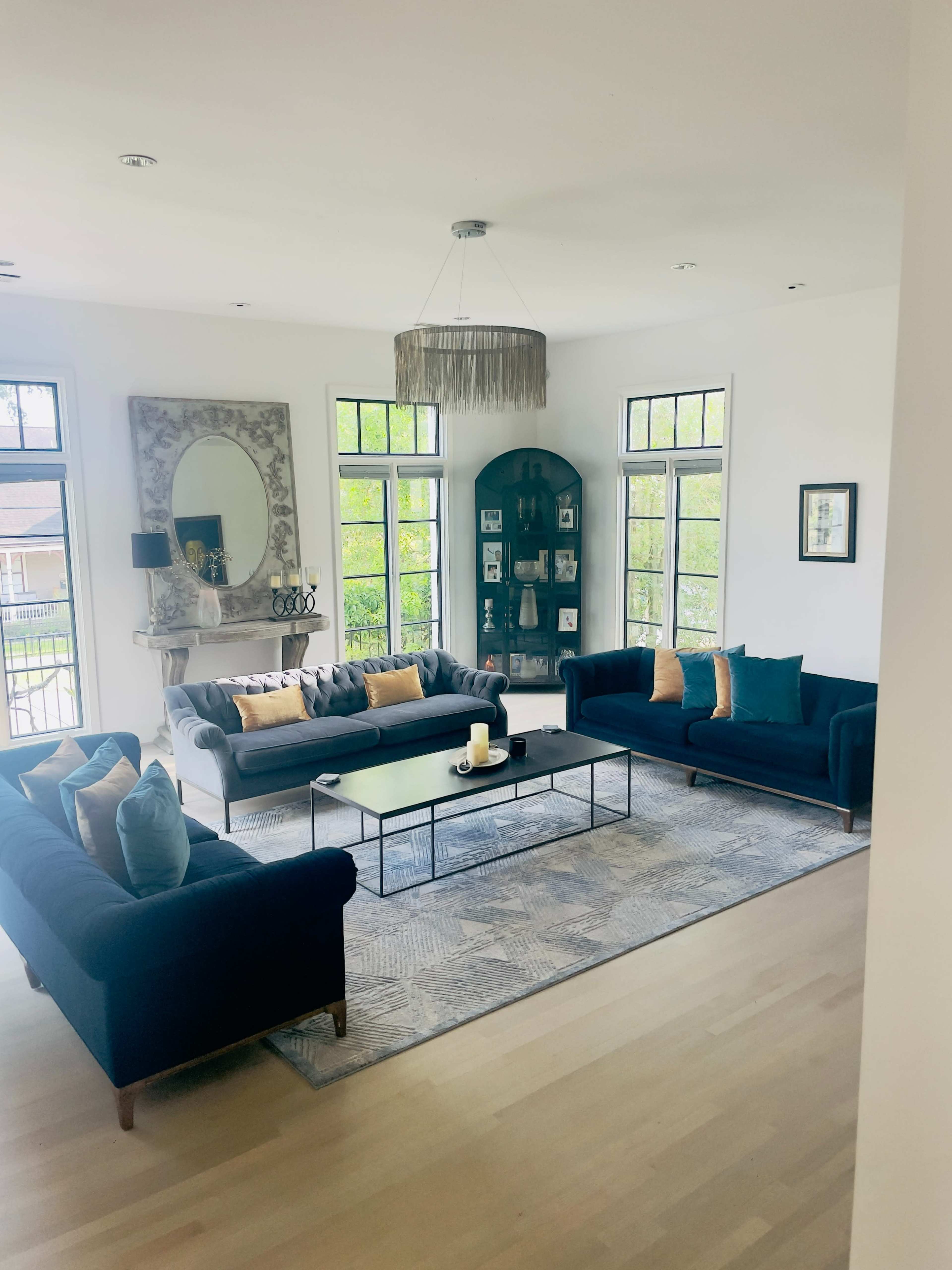 A modern living room features two dark sofas, a central glass coffee table, and large windows allowing light to fill the space.