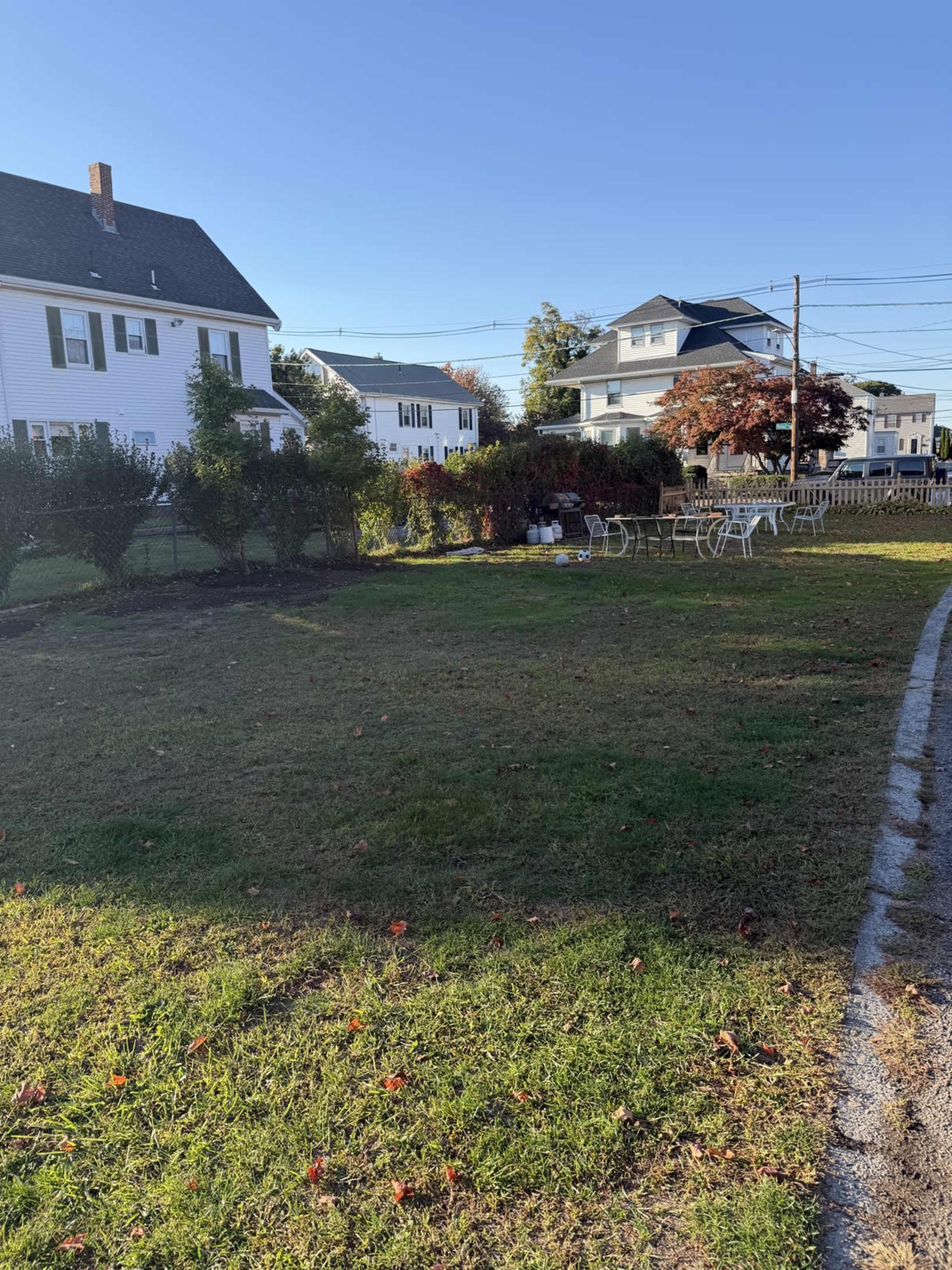 The image shows a grassy yard with a few chairs and houses in the background under a clear blue sky.