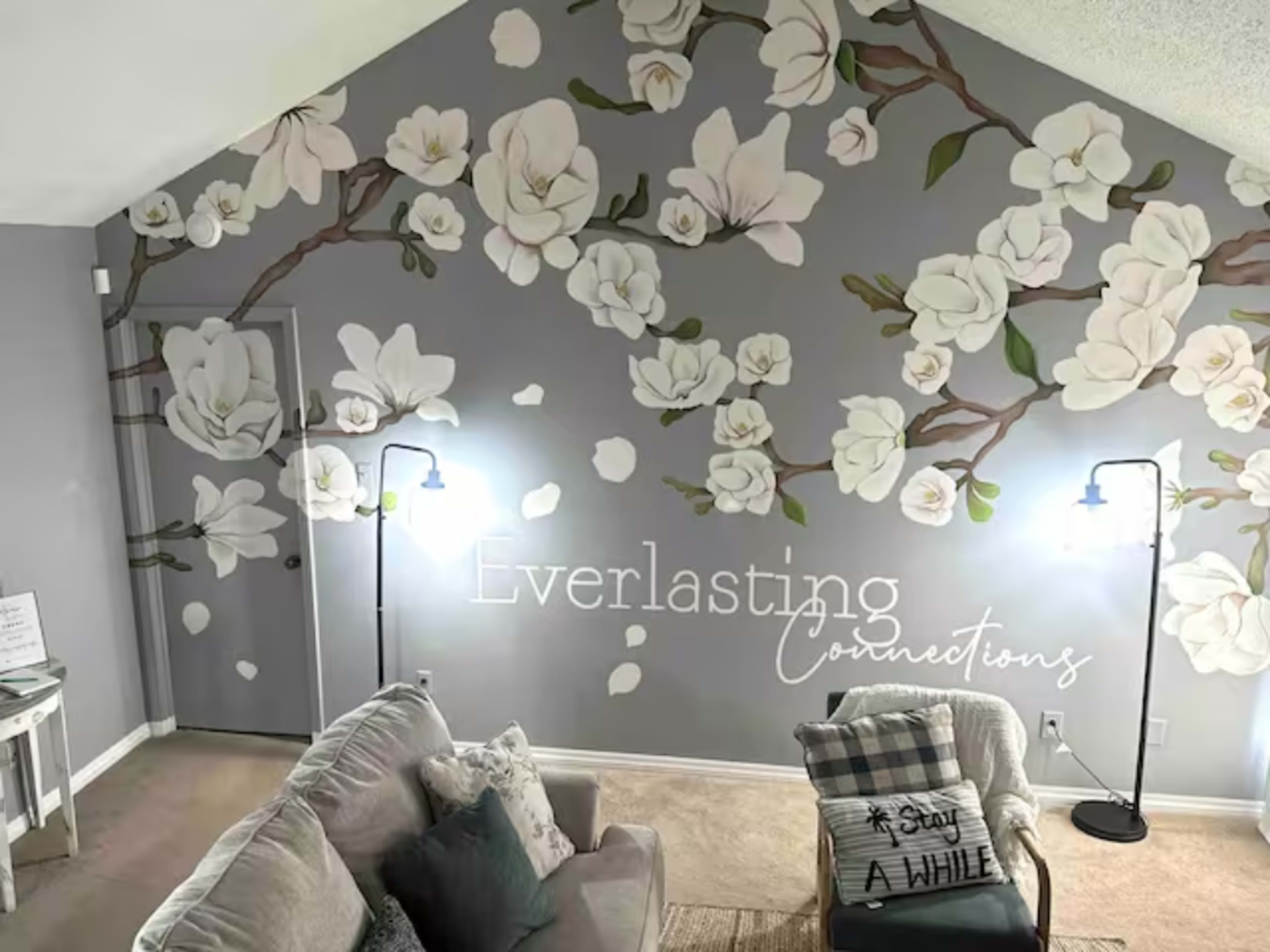 A living room features a large mural of white flowers on a grey wall, accompanied by a couch and decorative items.