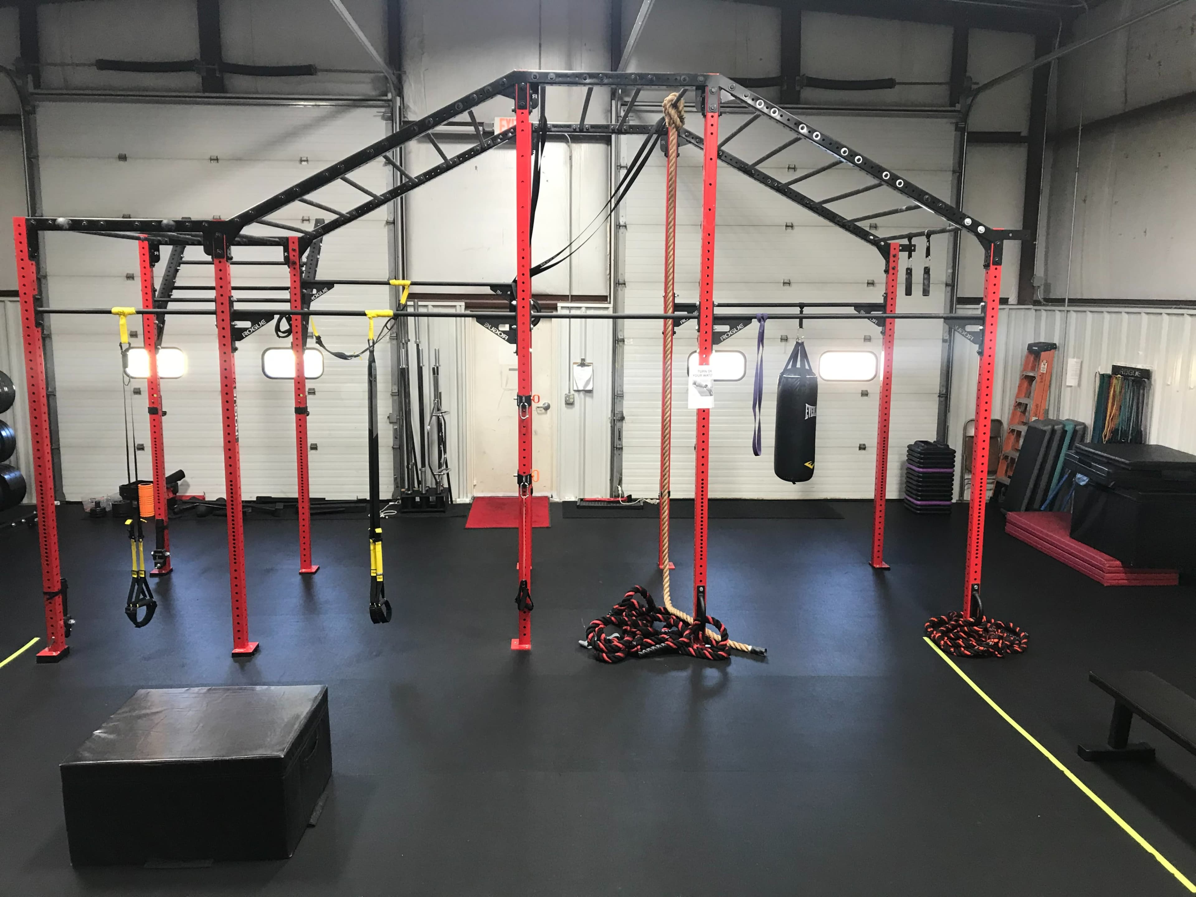 A gym facility equipped with a multifunctional training rig, suspension straps, a heavy bag, and various fitness equipment on a rubber flooring surface.
