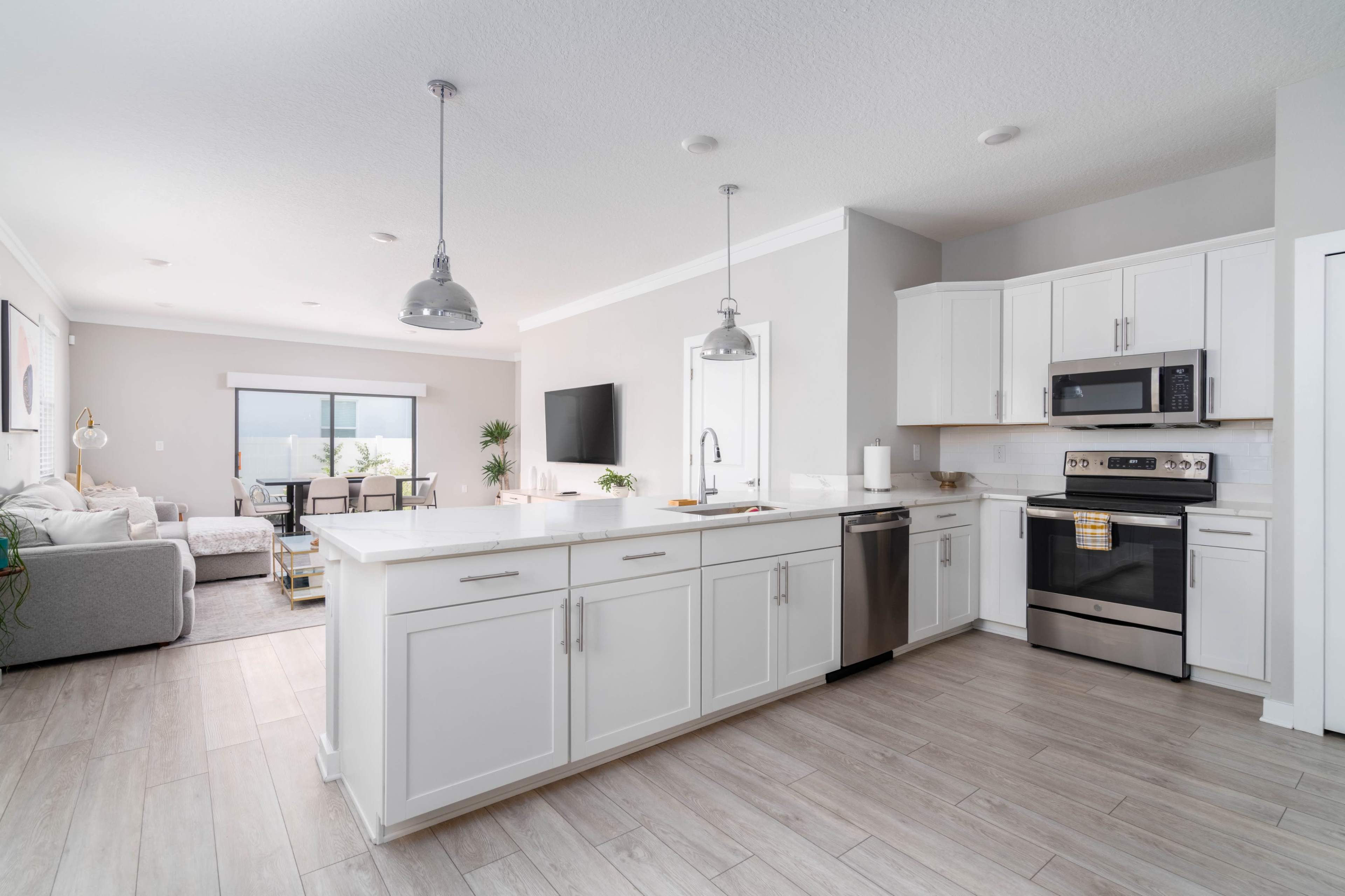 A modern kitchen with white cabinets, stainless steel appliances, and an open layout connected to a living area.
