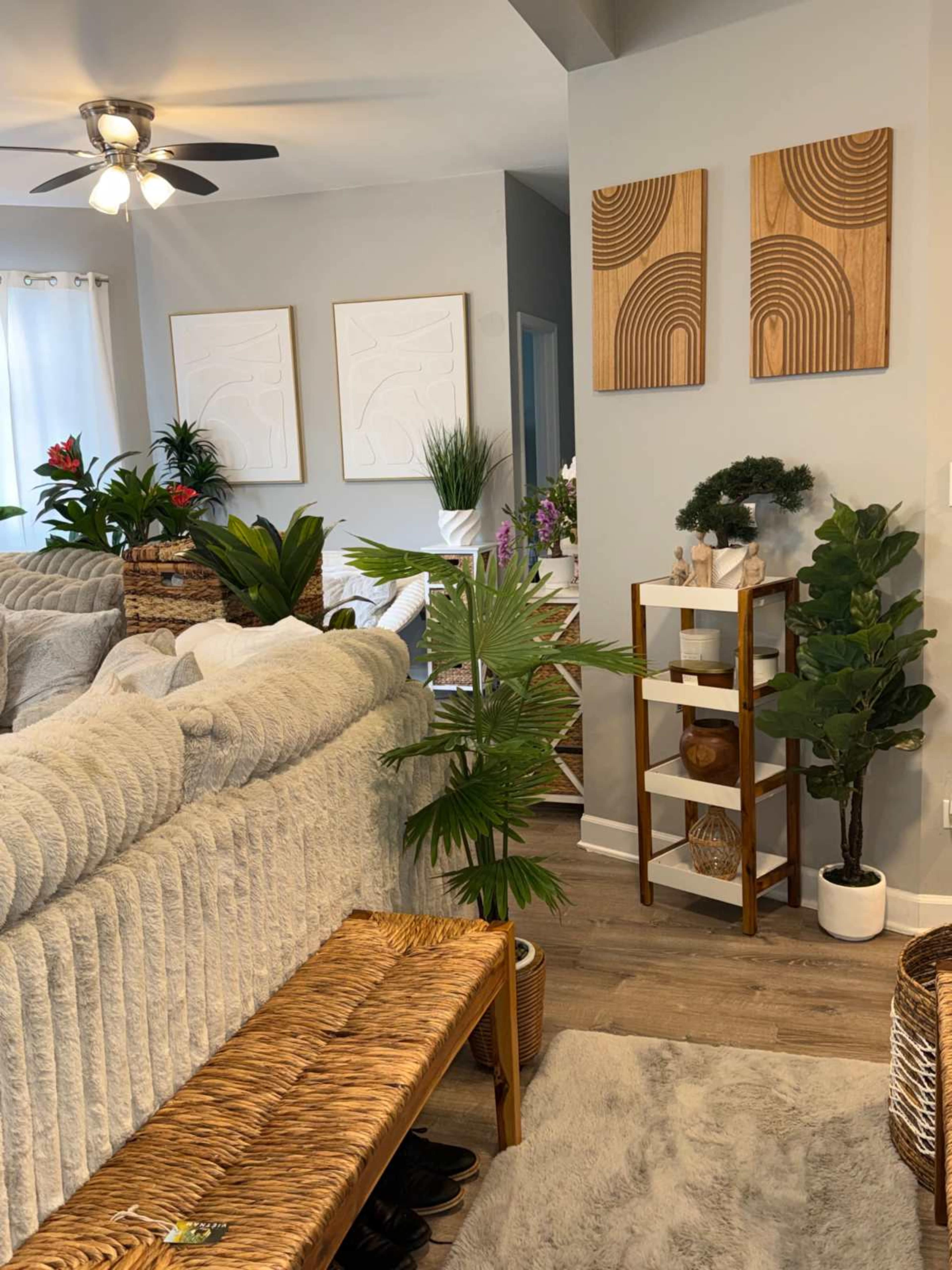 The image shows a cozy living area with a light gray sofa, decorative plants, and wall art featuring circular designs.