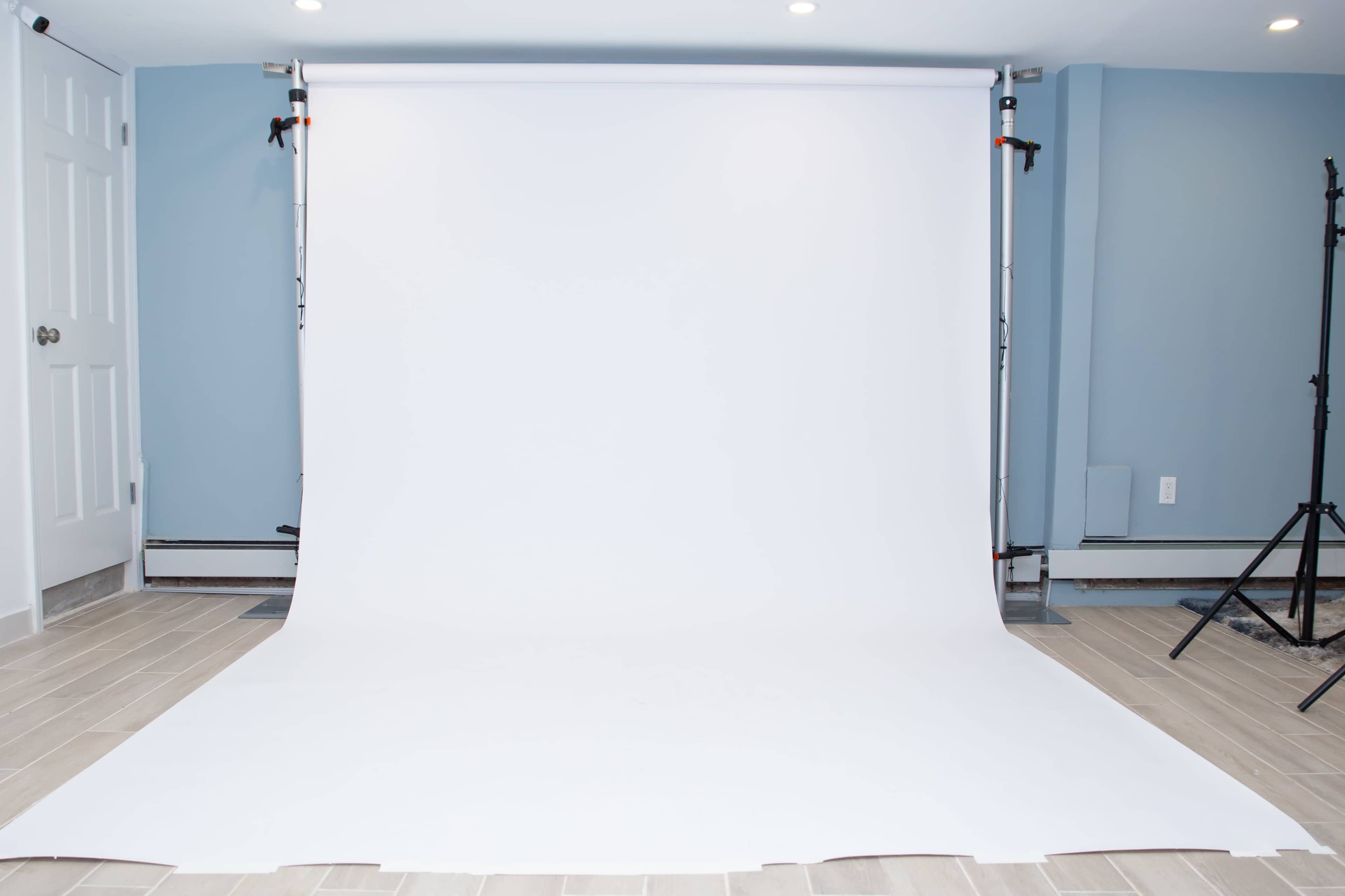 A clean, white backdrop is set up in a room with blue walls and tiled flooring, ready for photography.