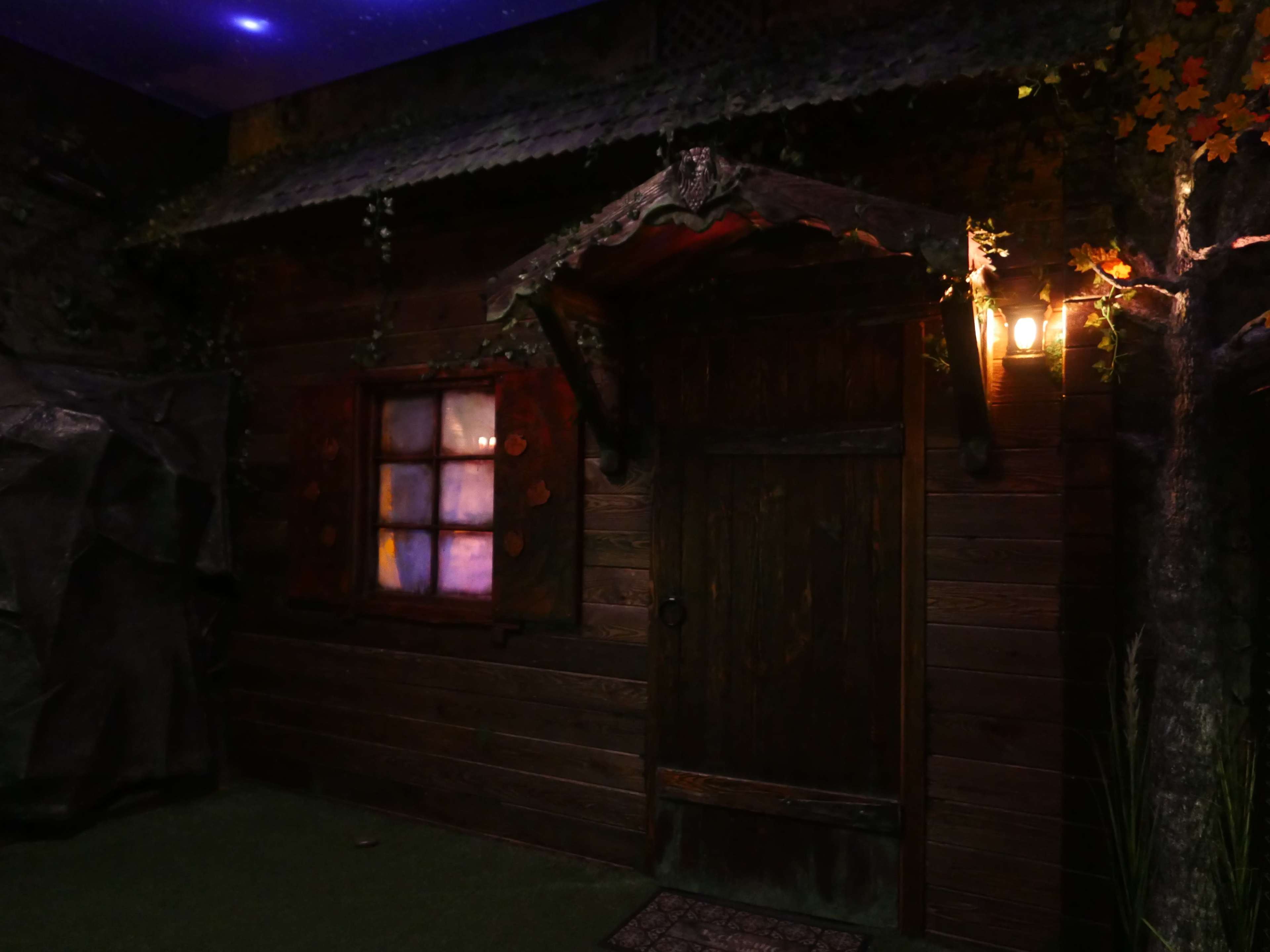 The exterior of a rustic wooden cabin with a door and a window, illuminated by a nearby light.