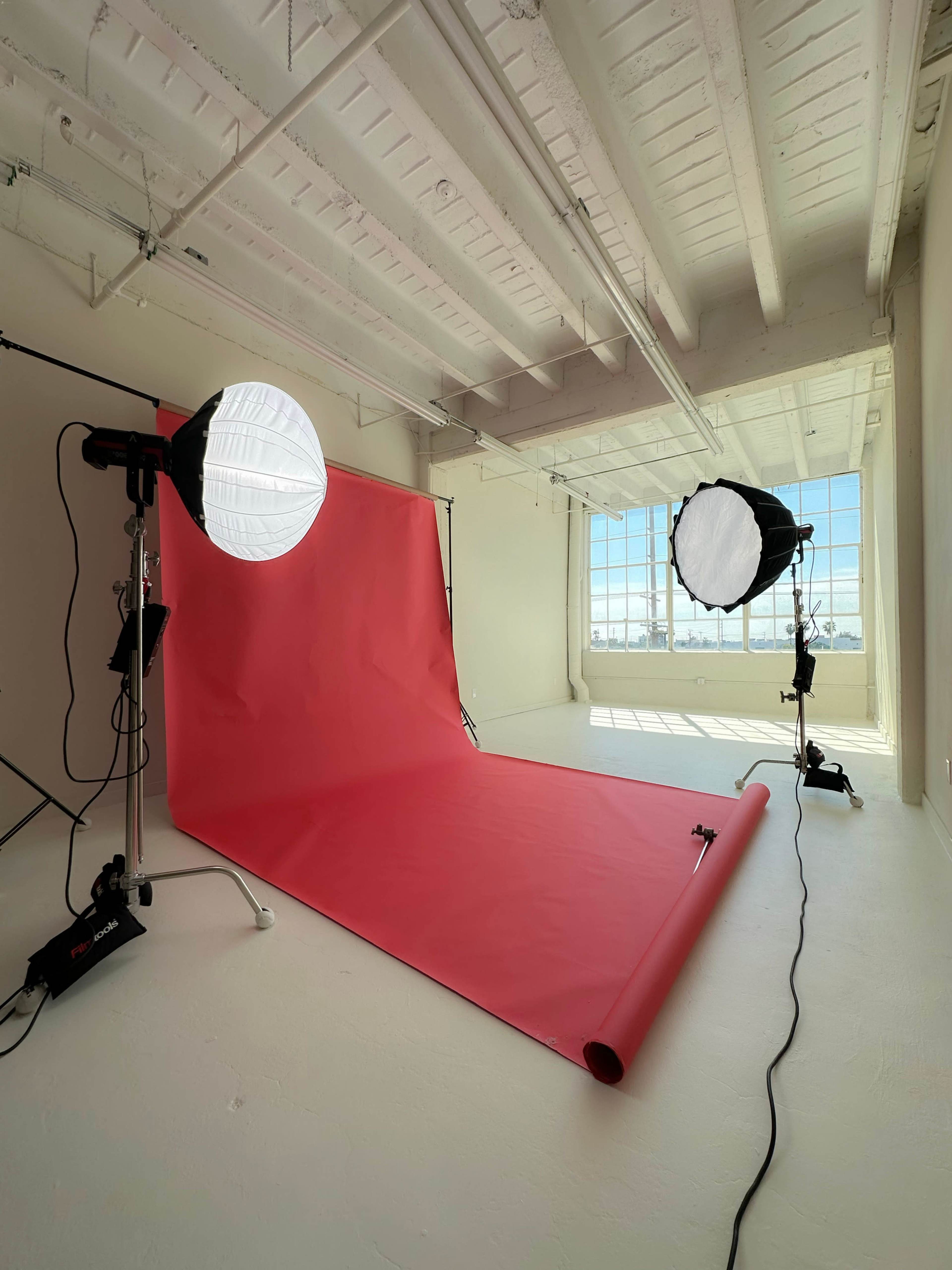 A photography studio with a red backdrop and two softbox lights set up in a bright, spacious room.