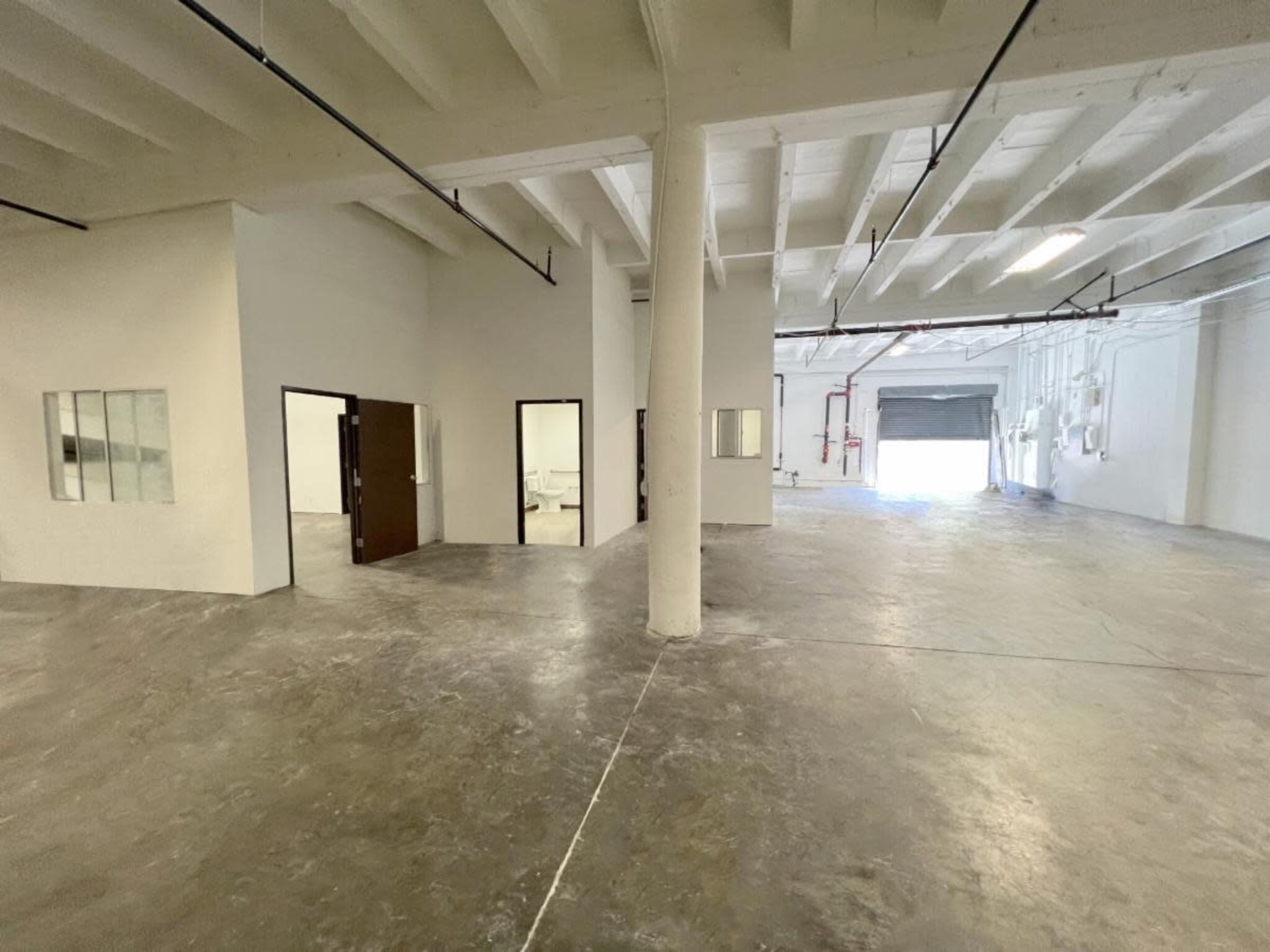 The image shows a spacious, unfinished industrial area with concrete floors and multiple doorways leading to separate rooms.