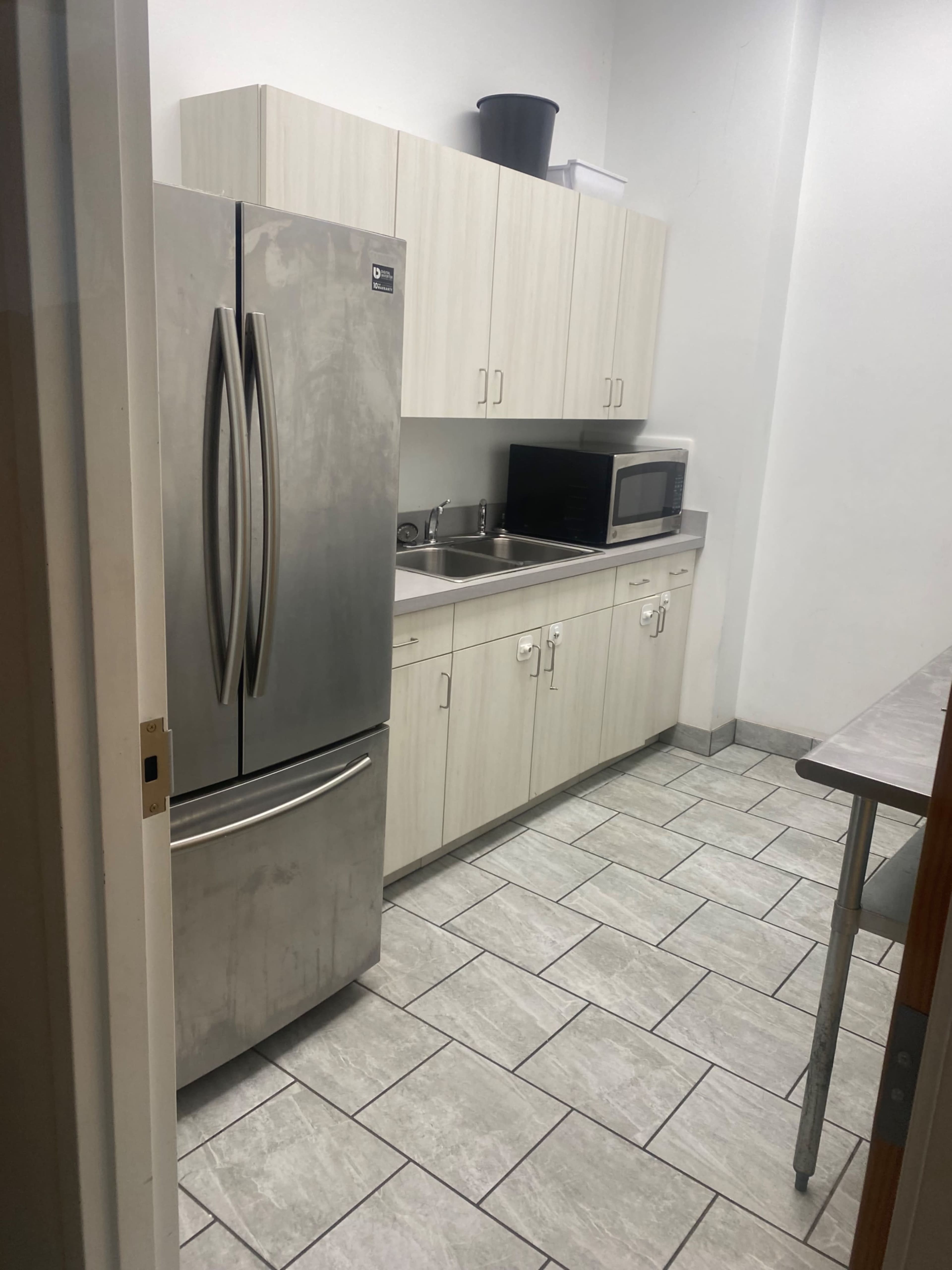A small kitchen area features a stainless steel refrigerator, wooden cabinets, a microwave, and a countertop with a sink.