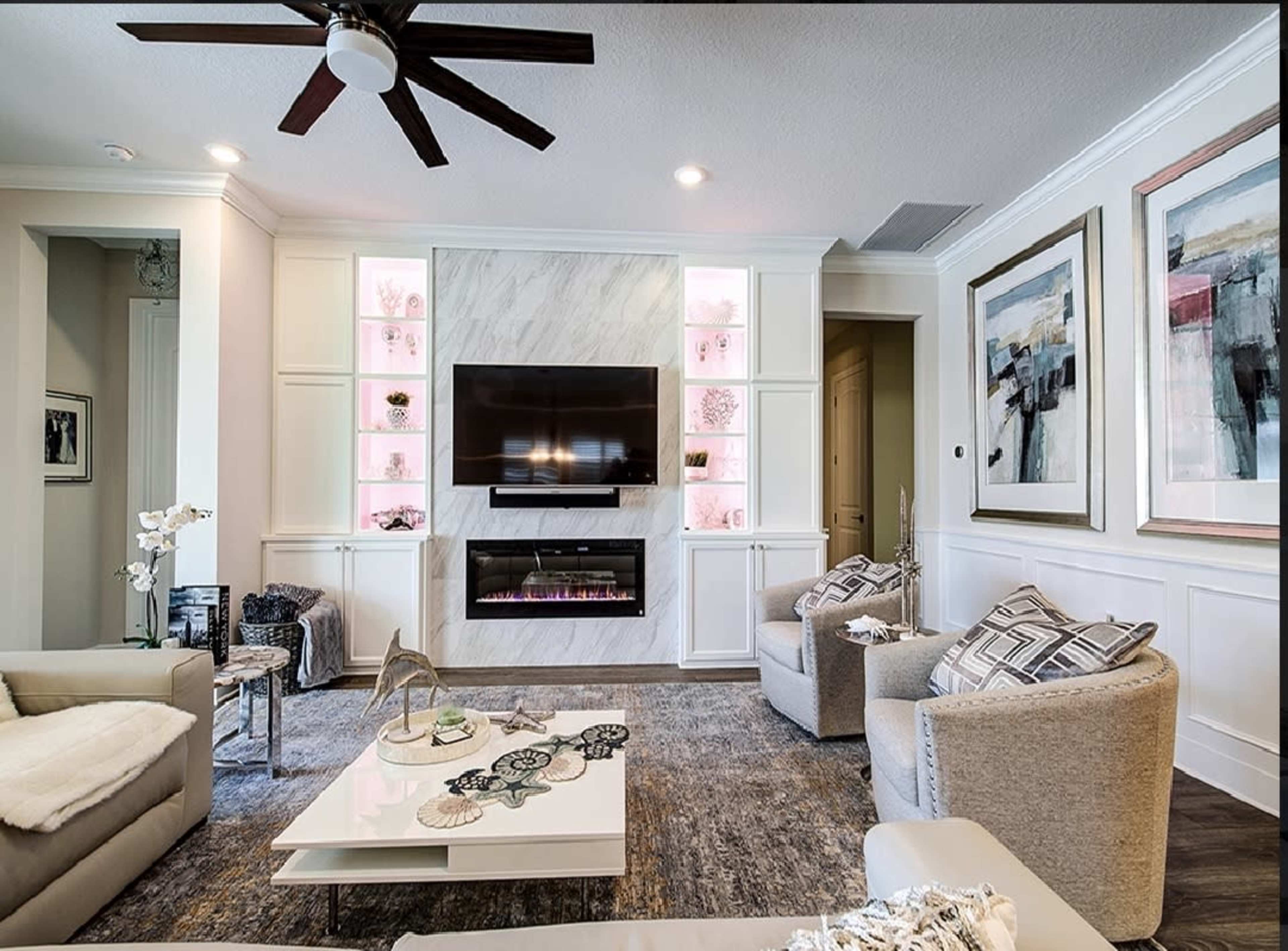 A modern living room with a wall-mounted TV above a fireplace, flanked by built-in shelves displaying decorative items and illuminated with soft lighting.