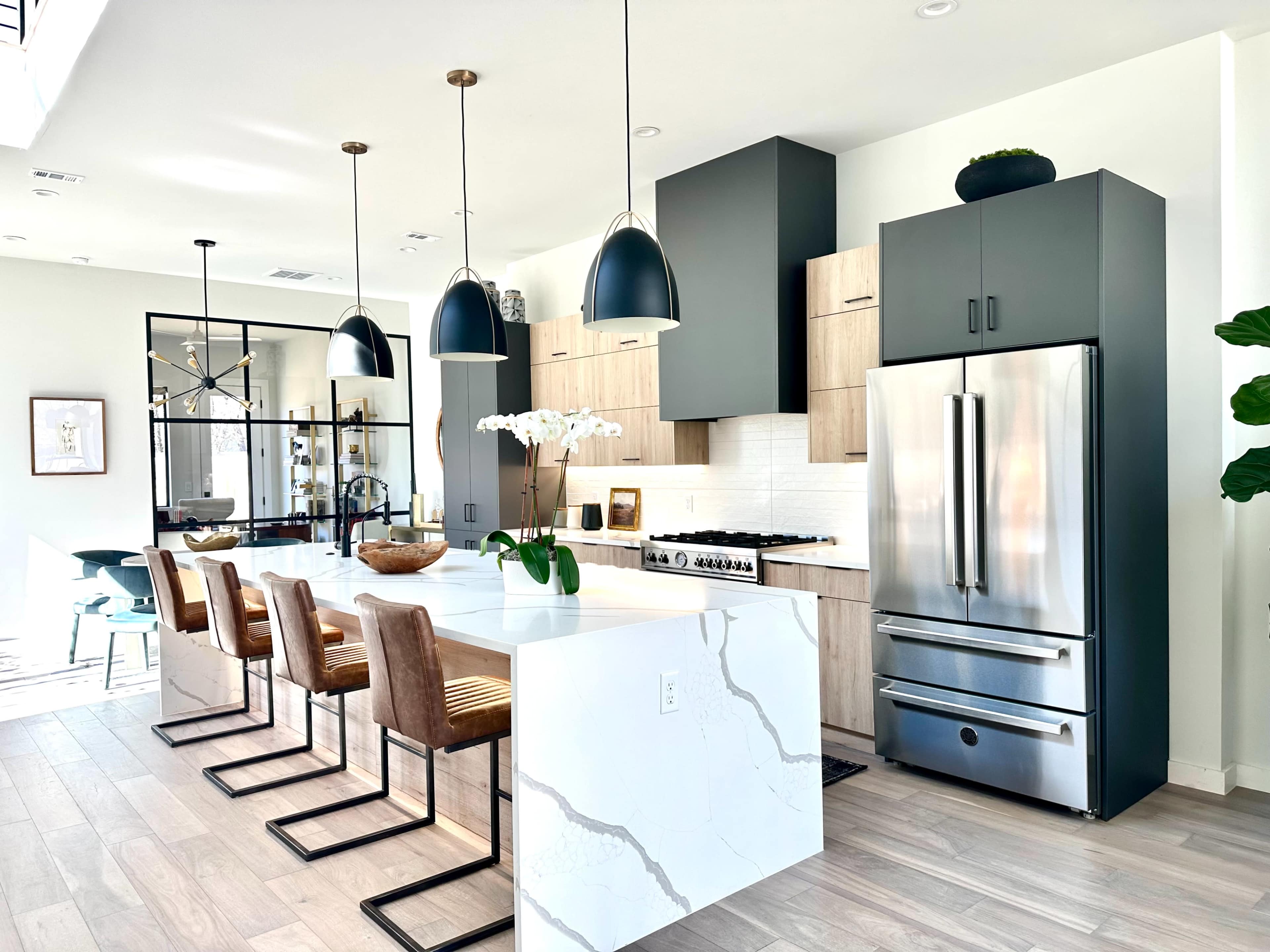 A modern kitchen featuring a large island with four stools, stainless steel appliances, and pendant lighting, complemented by light wood and dark cabinetry.