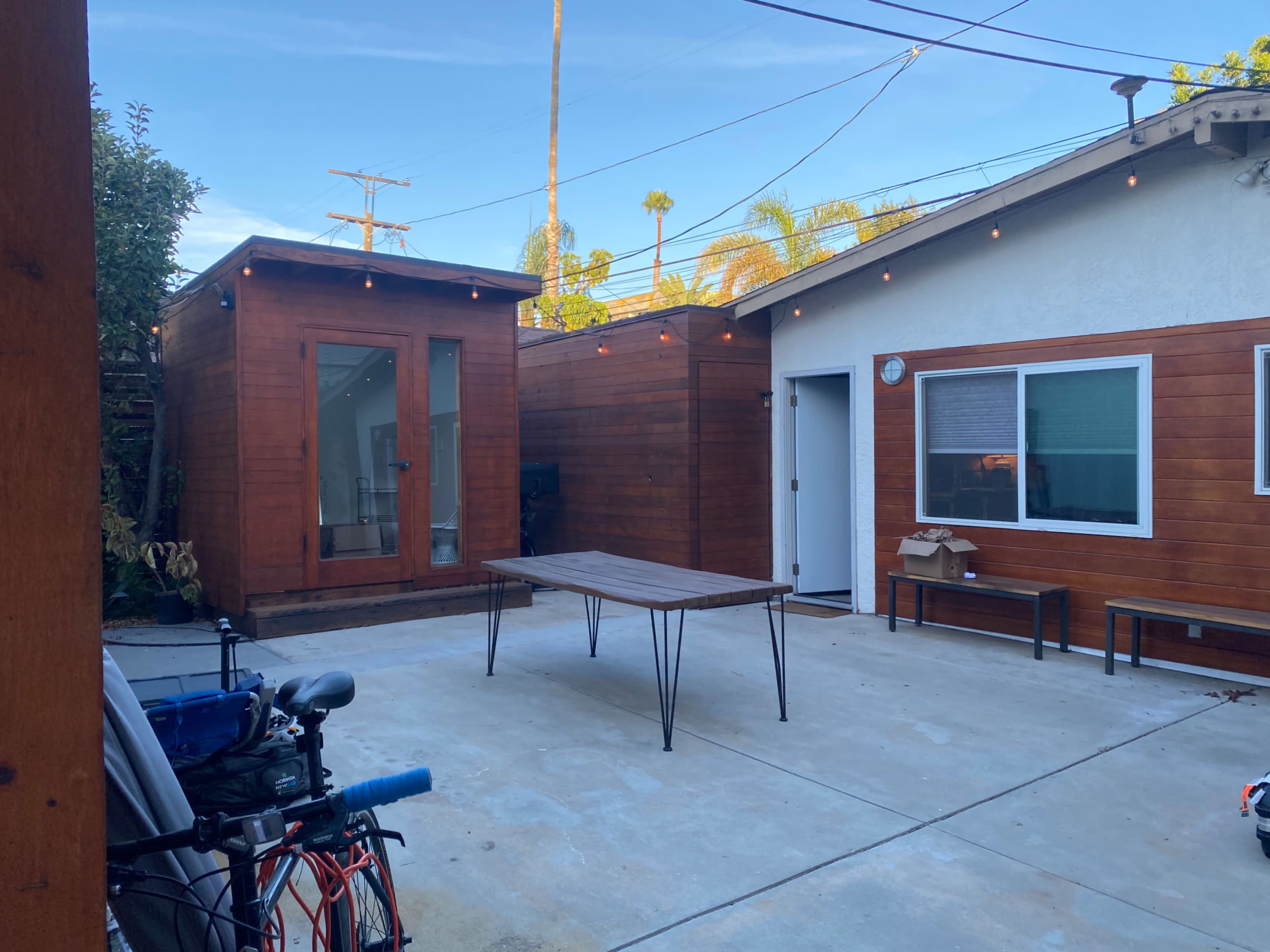 A courtyard with a wooden table, surrounded by buildings made of wood siding, and string lights overhead.