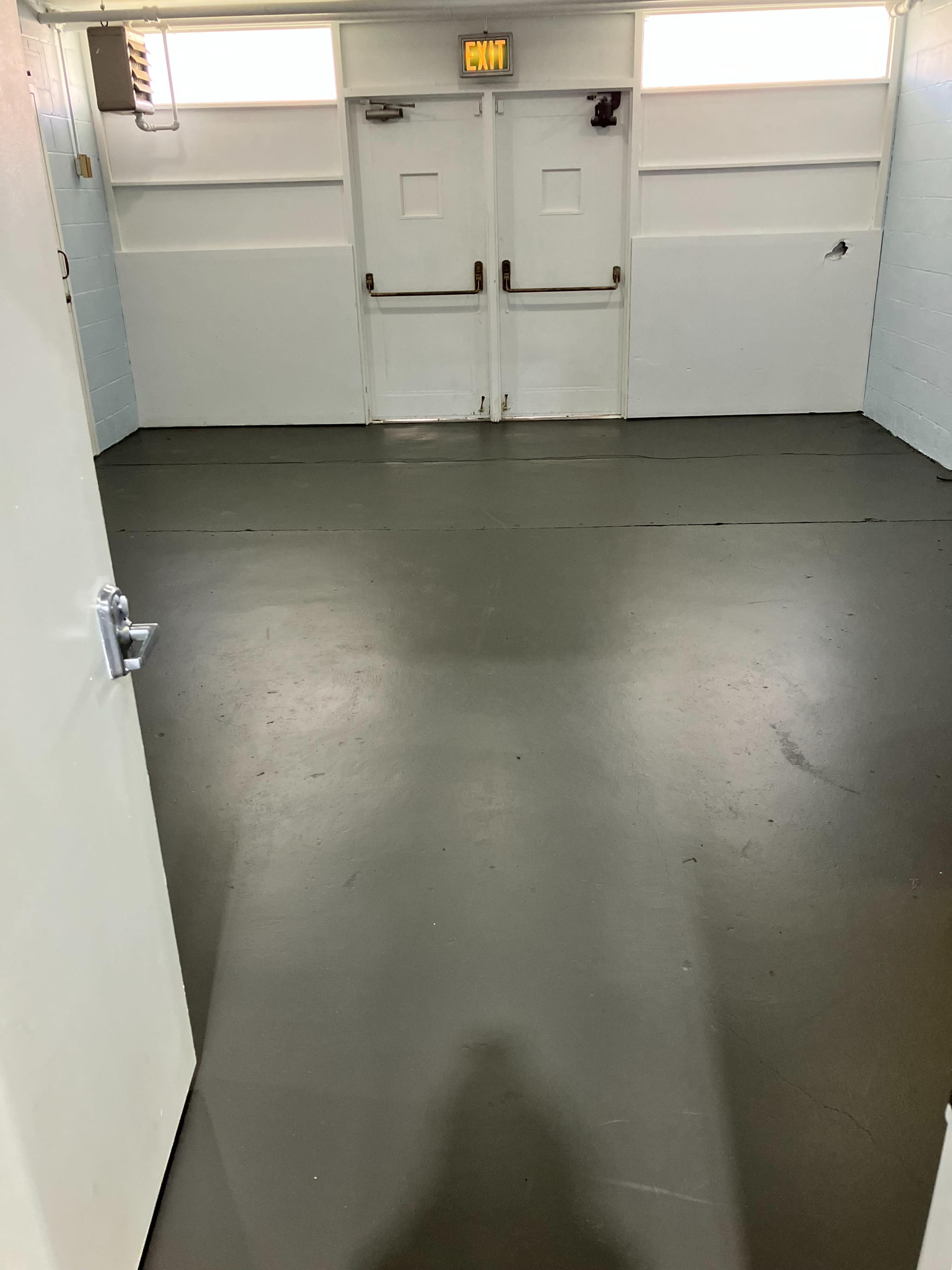 The image shows a simple, empty room with a gray floor and double doors at the far end.