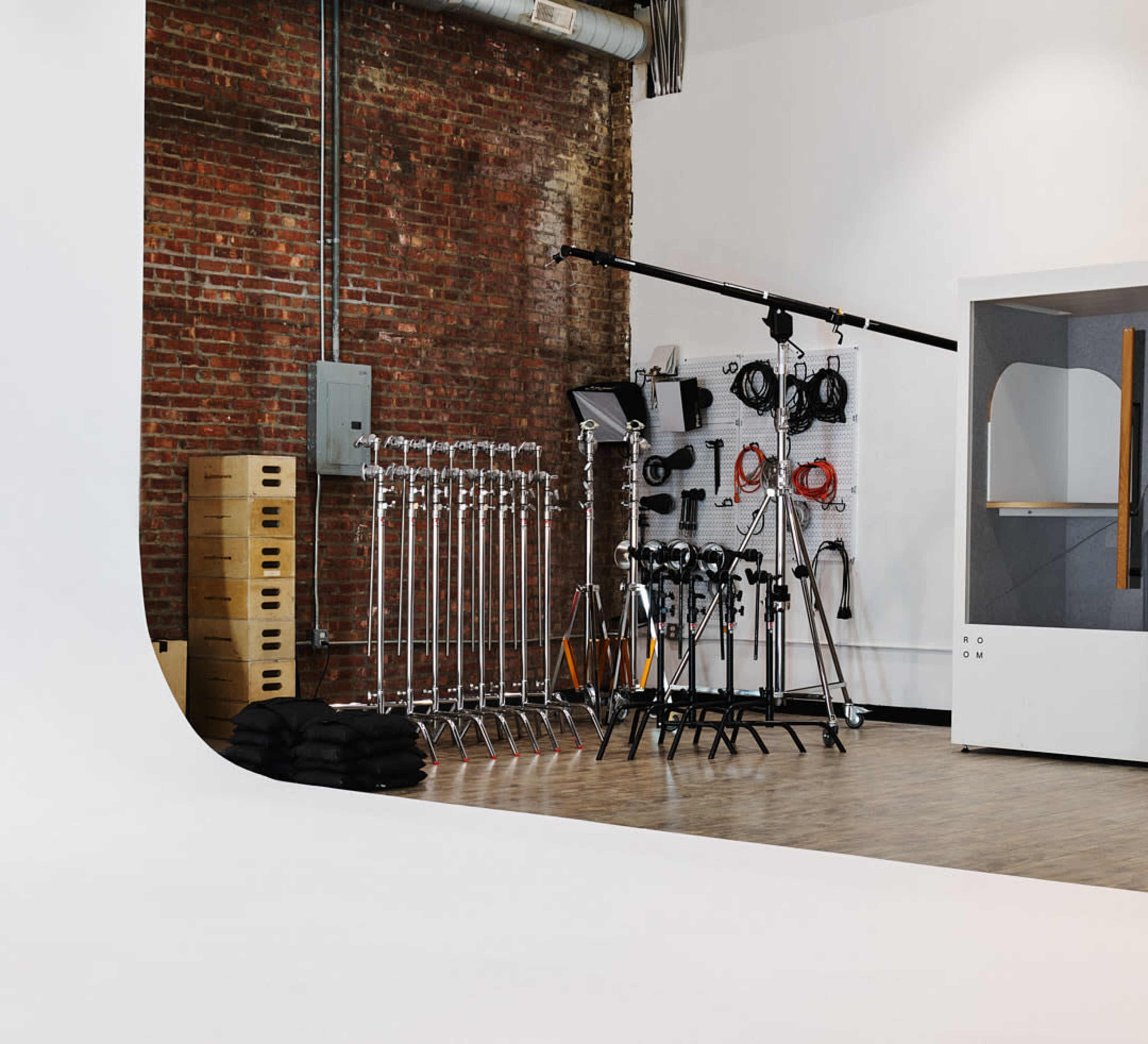 A photography studio with a seamless white backdrop, various stands and equipment, and storage boxes against a brick wall.