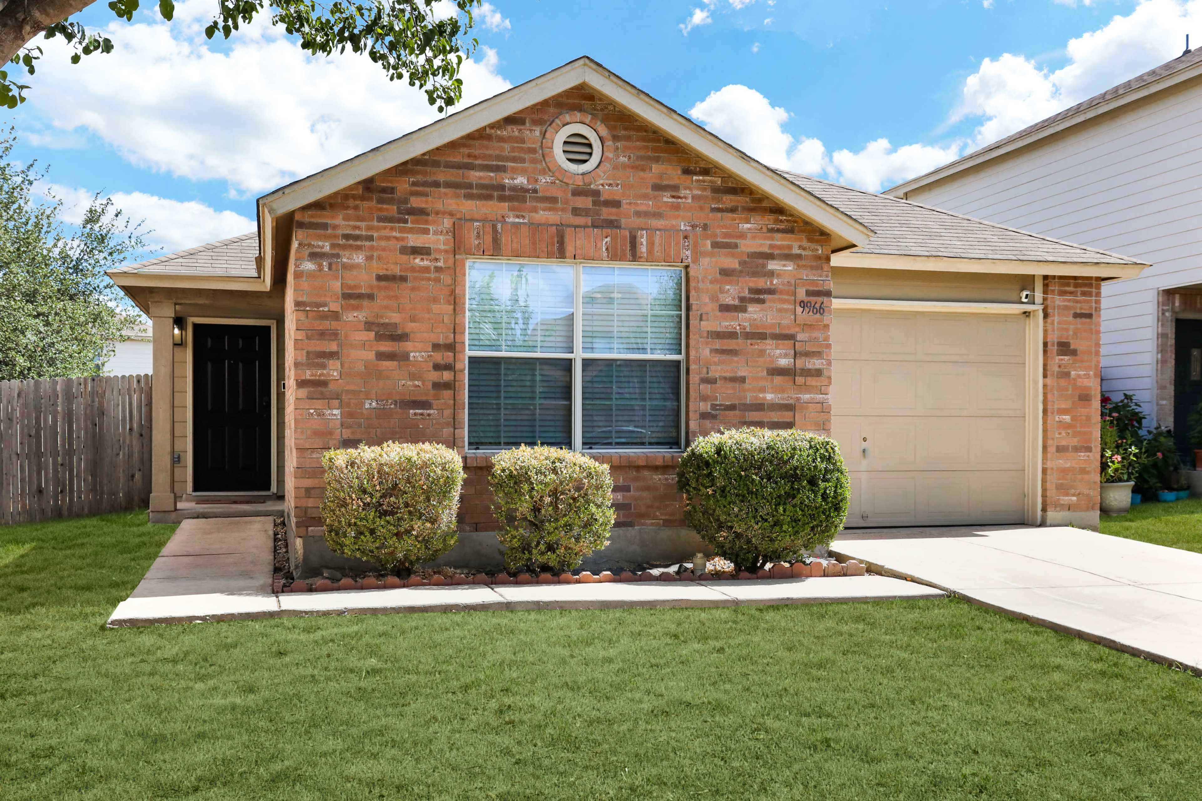 A single-story brick house with a front lawn, two shrubs by the entrance, and a single-car garage.