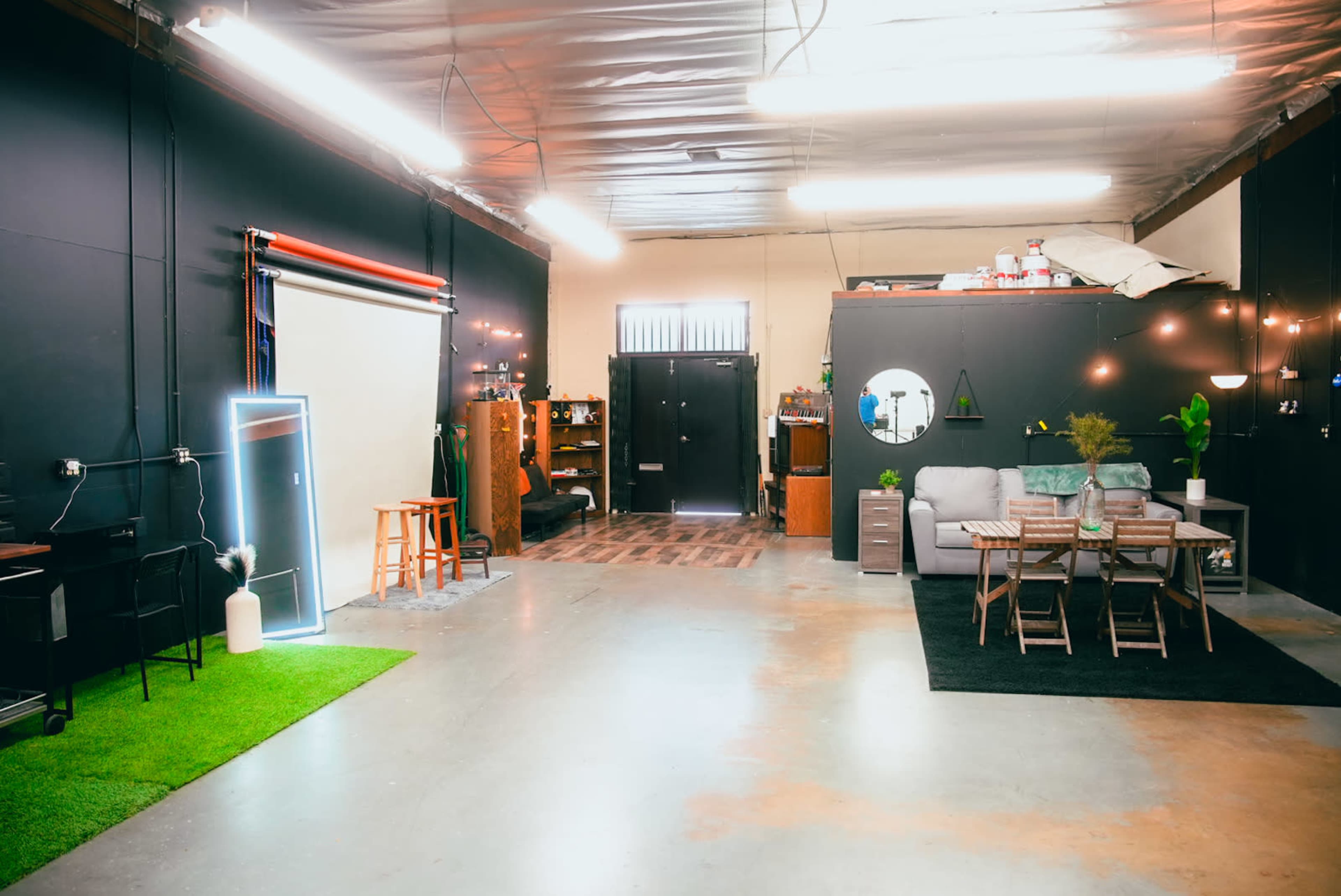 A spacious interior with a divided area featuring a seating arrangement, a dining table, and decorative elements, along with a green patch of faux grass and a backdrop setup.