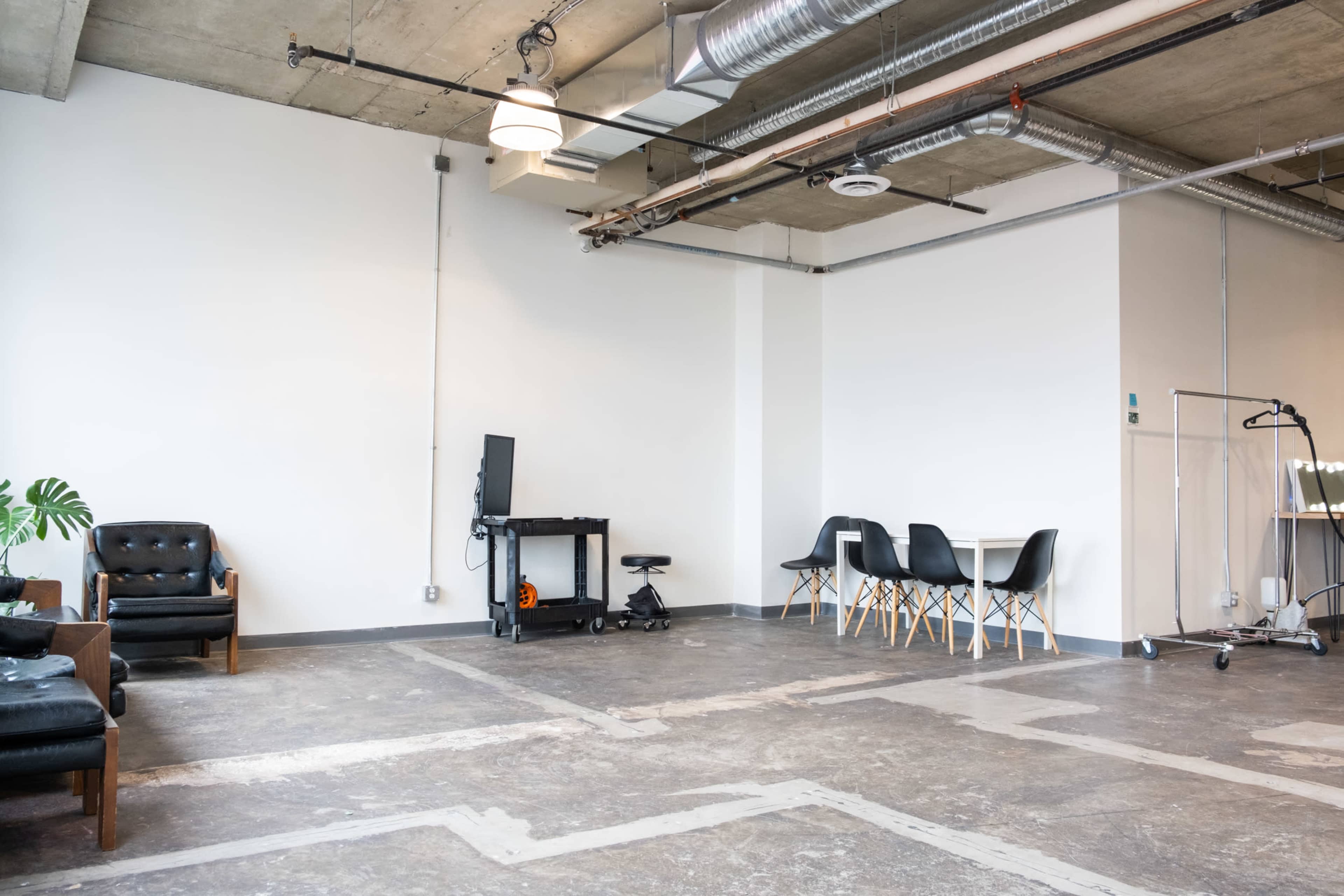 A spacious, minimalist interior with a seating area, a workstation, and a dining table set against a plain wall.