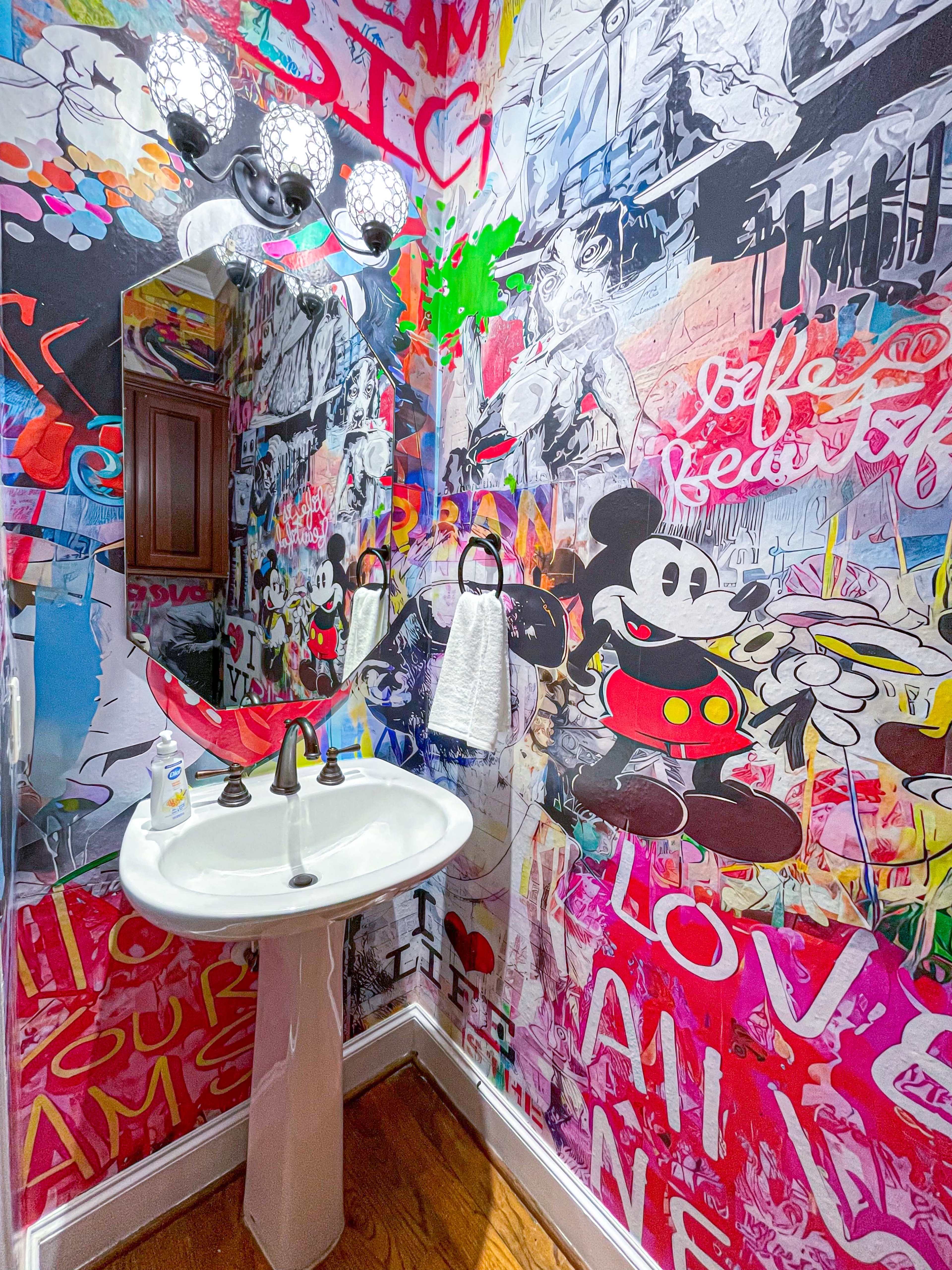 The bathroom features a sink mounted on a colorful, graffiti-style mural that includes images of Mickey Mouse.