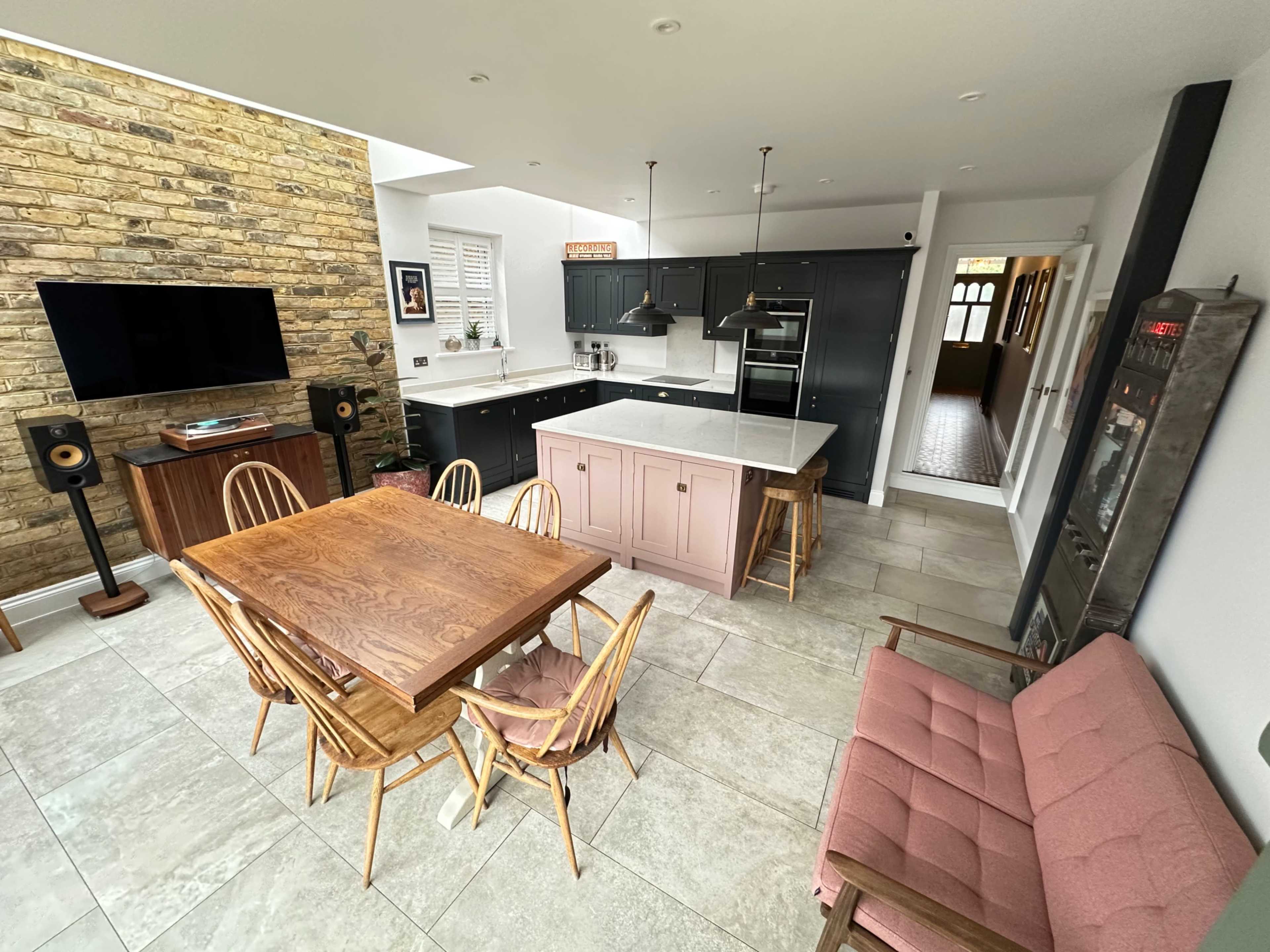 The image shows a modern kitchen and dining area with a large wooden table, stylish chairs, and a stone accent wall.