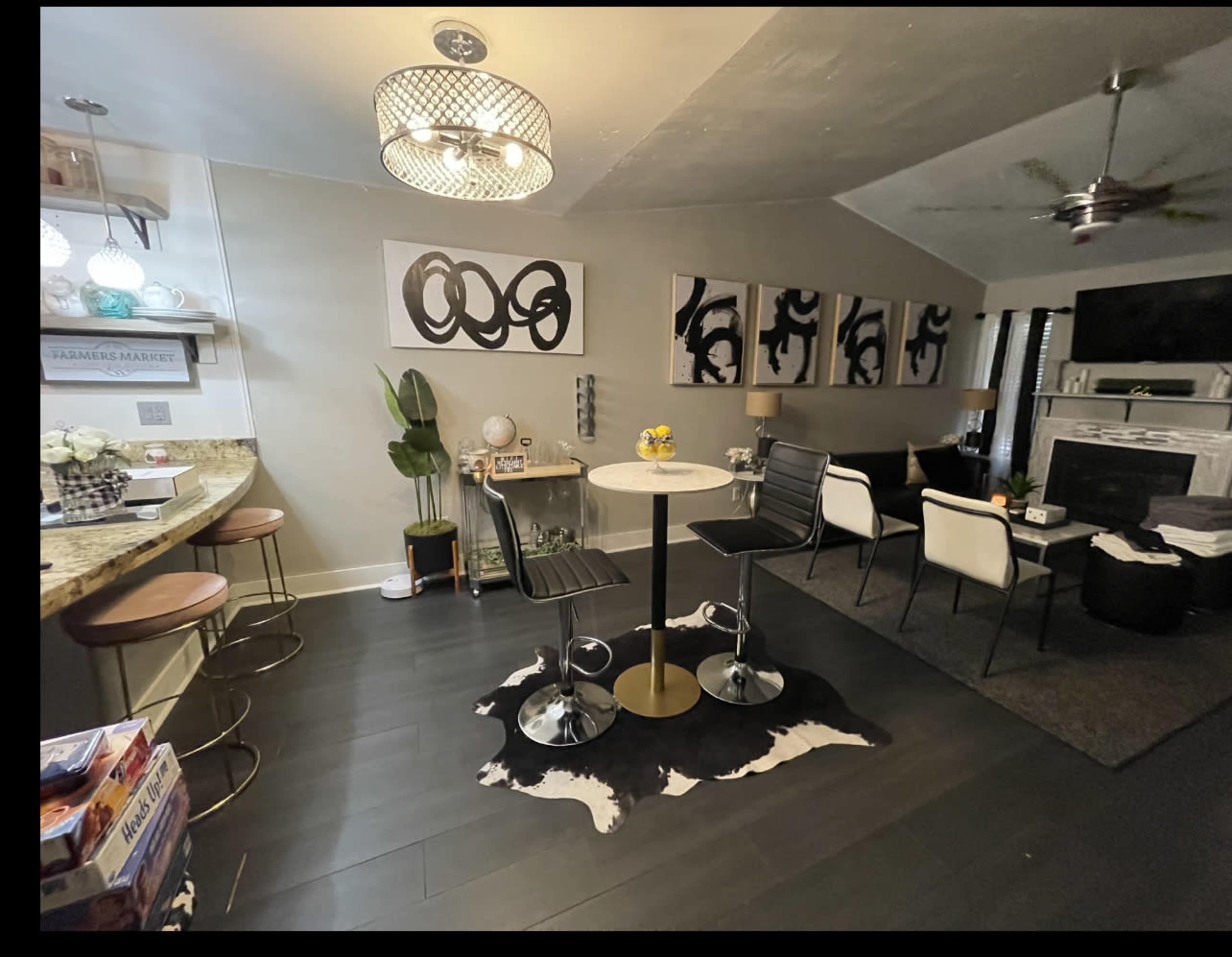 A modern living room and kitchen area featuring a circular table with two stools, a sectional sofa, and contemporary artwork on the walls.