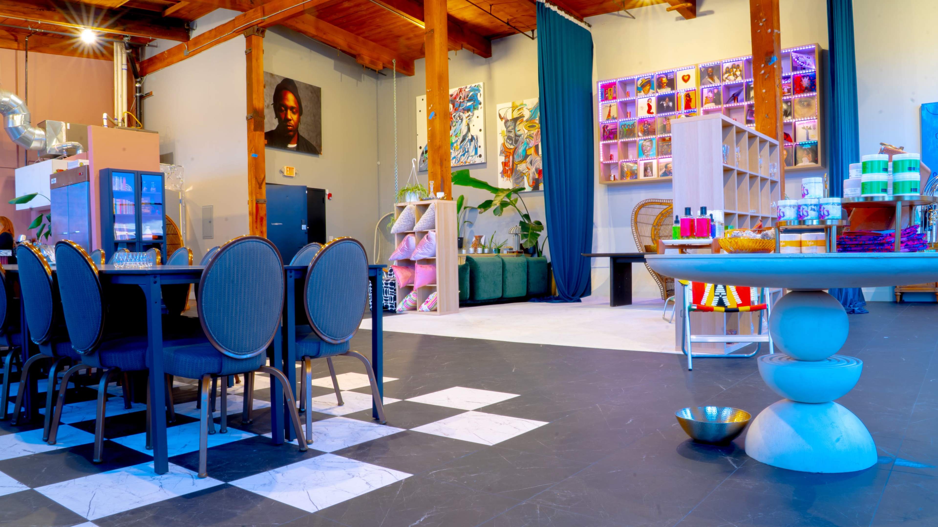 The image shows a spacious interior featuring a dining area with a large black table and upholstered chairs, surrounded by colorful decor and art on the walls.