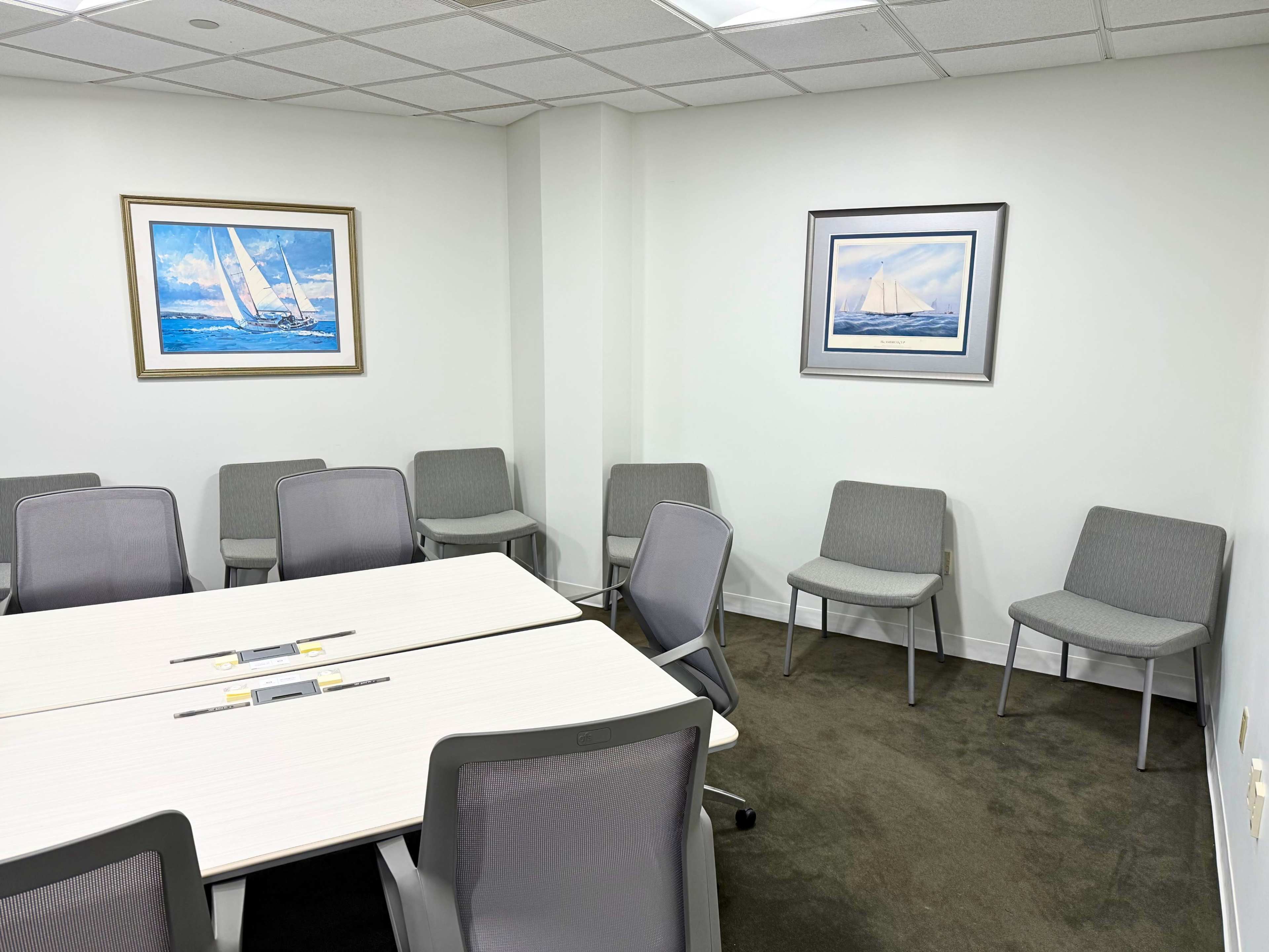 The image shows a well-lit meeting room with a large rectangular table surrounded by chairs and two framed nautical paintings on the walls.