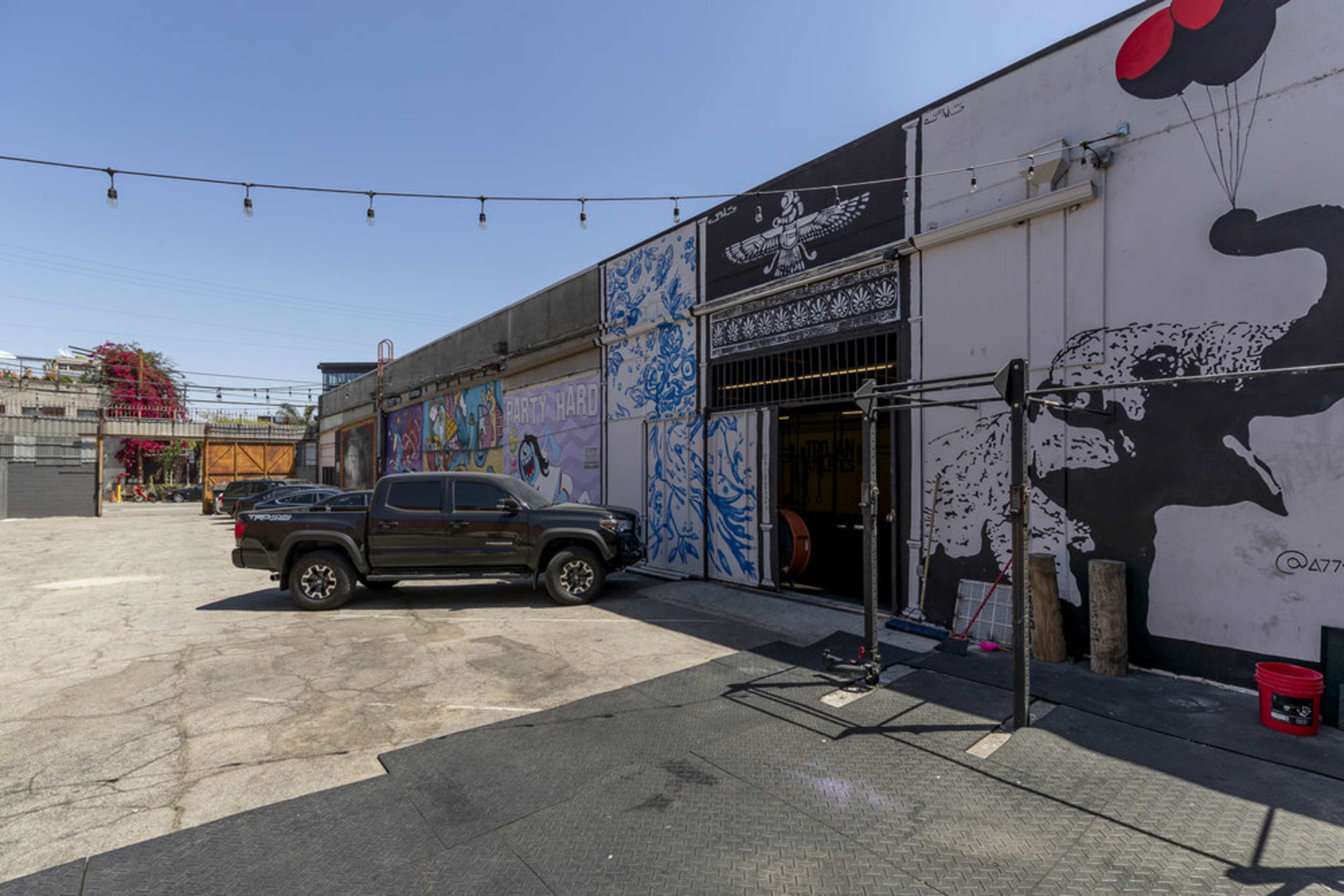 The image shows a parking area outside a building adorned with murals, featuring a black truck parked near an entrance.