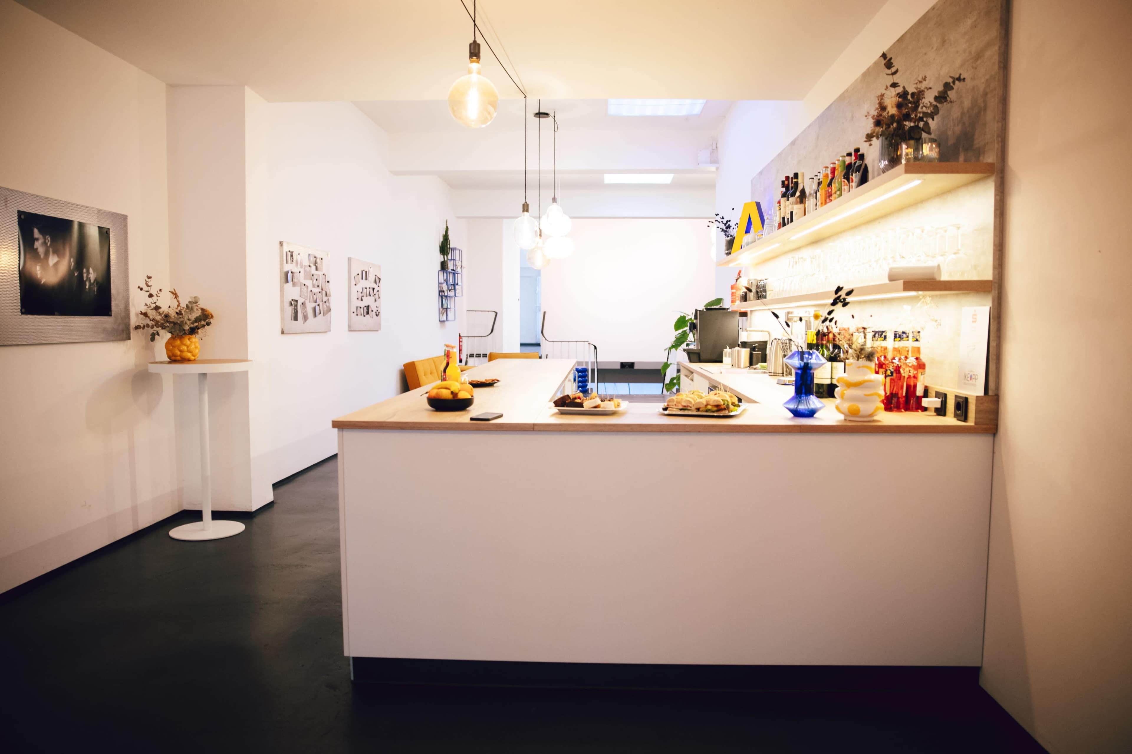 The image shows a modern kitchen area featuring a minimalist design with a wooden countertop, several decorative items, and soft lighting.