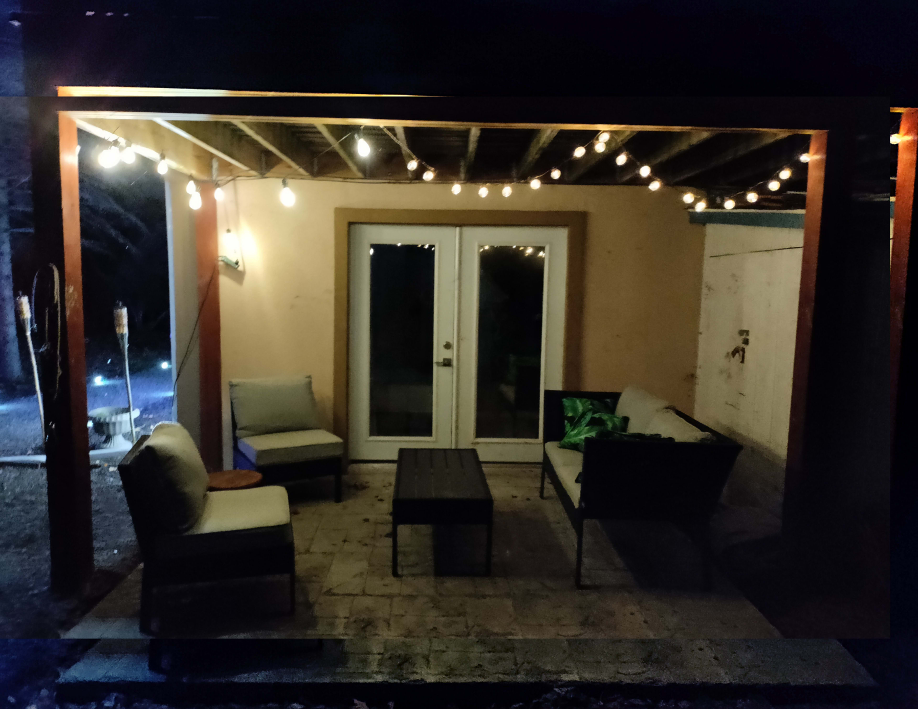 A covered patio area features string lights, a table, and seating arranged around it.