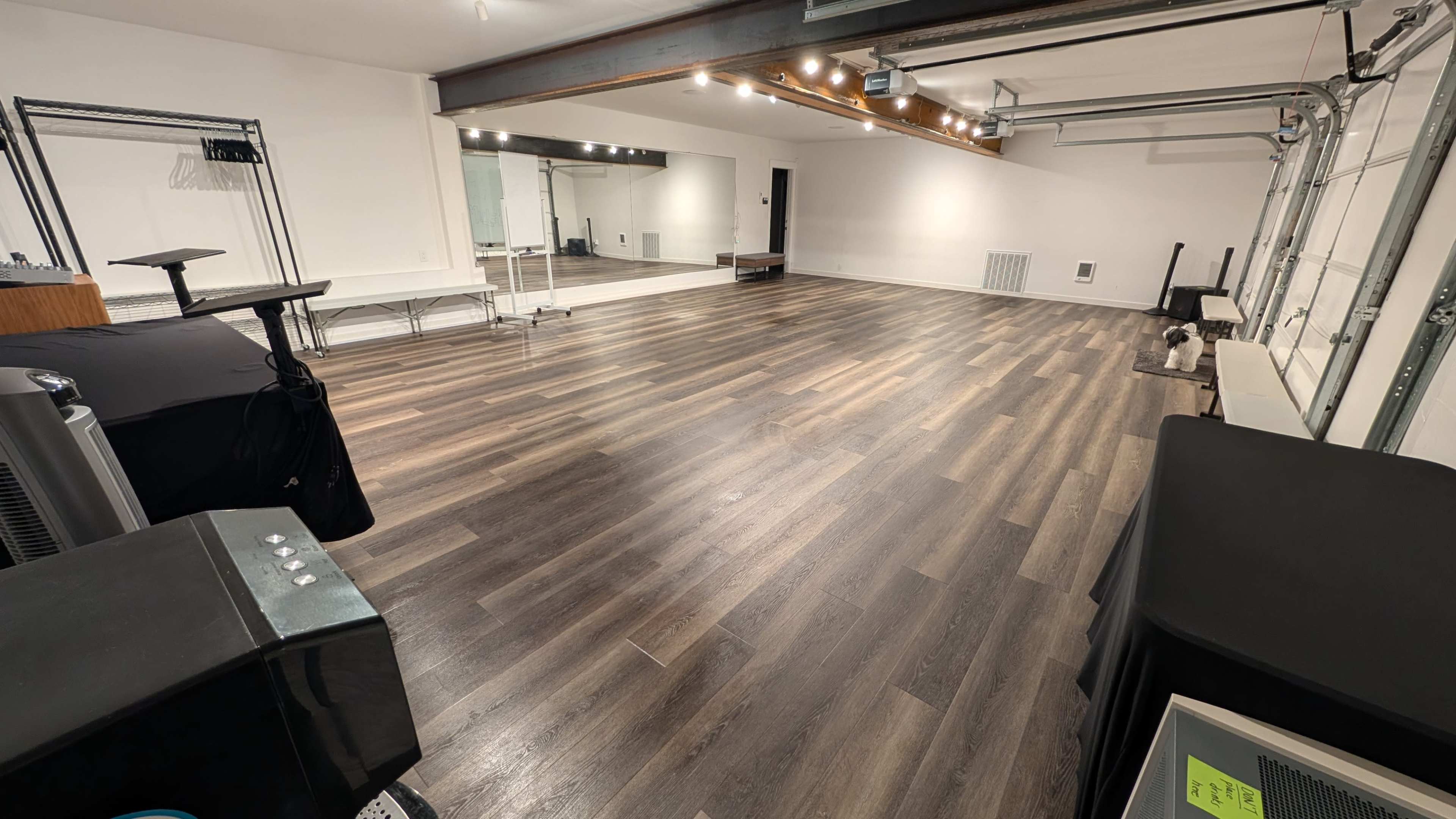 The image shows a spacious, empty room with wooden flooring and large mirrors on one wall.