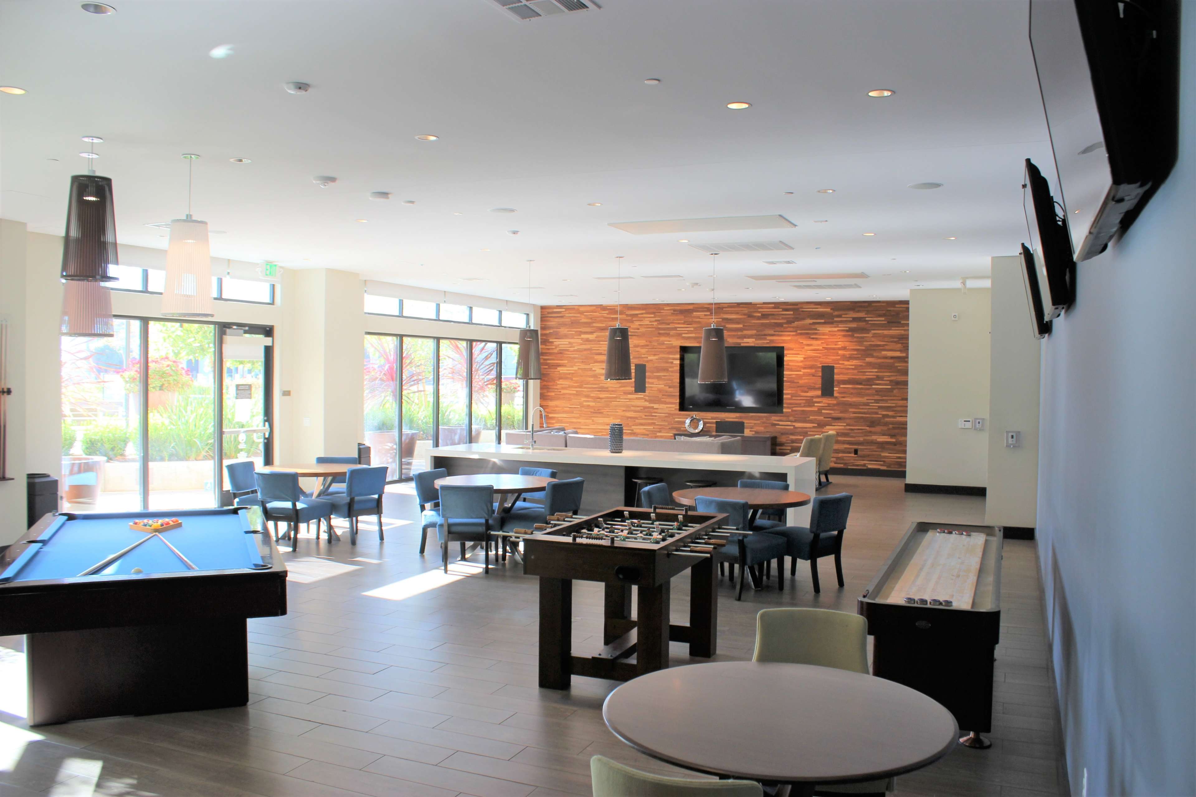A modern recreational room with a pool table, foosball table, and several seating areas, featuring large windows that provide natural light.