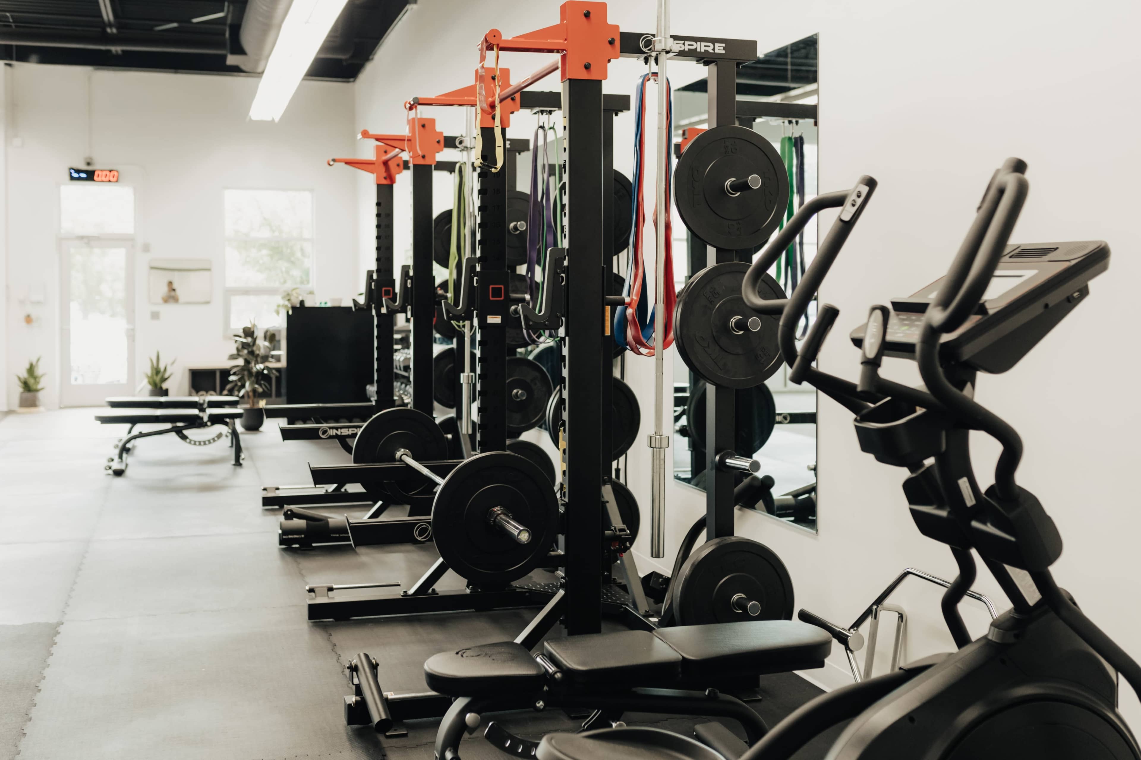 A fitness gym interior with weightlifting equipment, resistance bands, and exercise machines arranged along the walls.