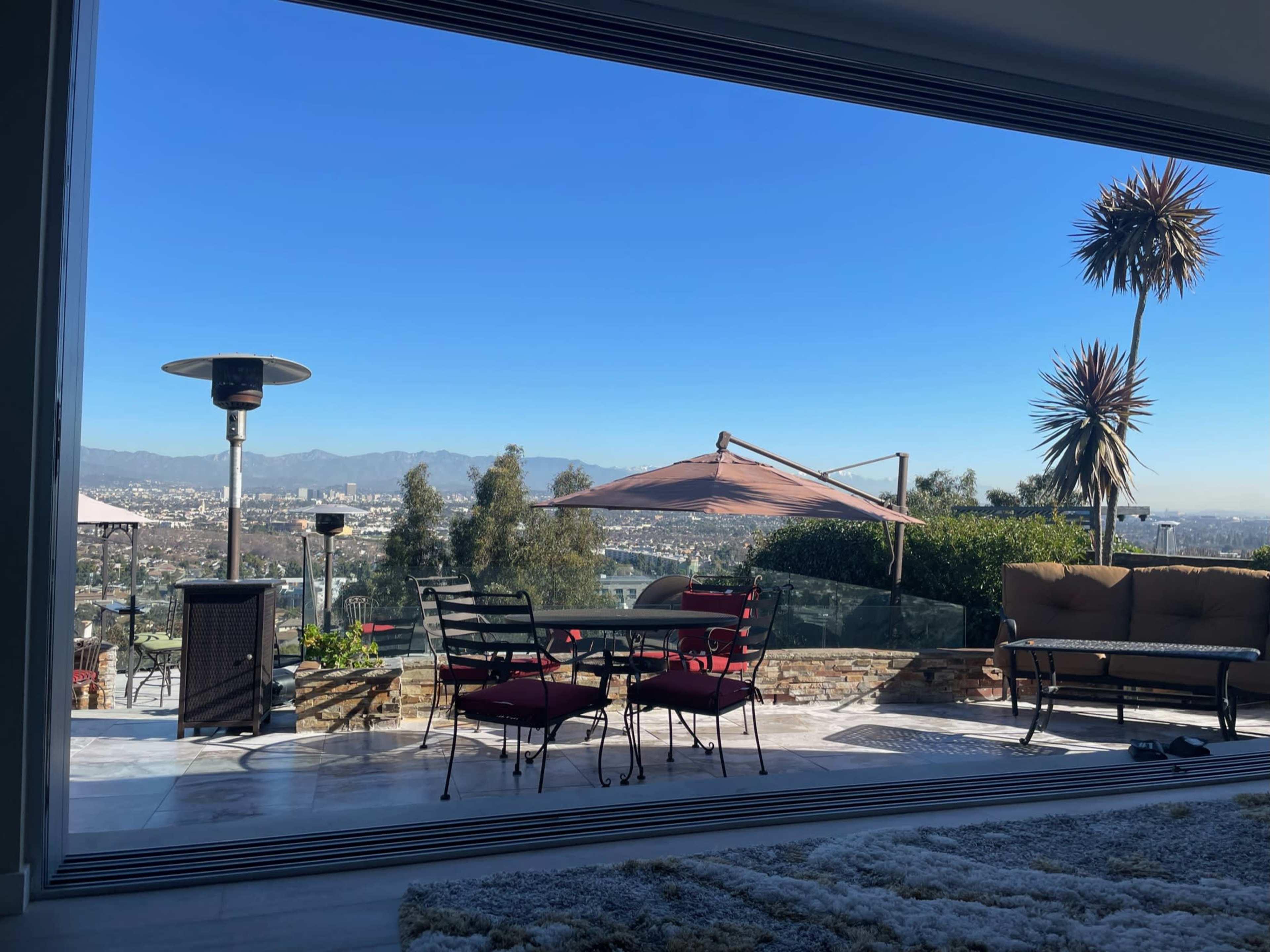 A patio with a table and chairs overlooks a cityscape and mountains under a clear blue sky.