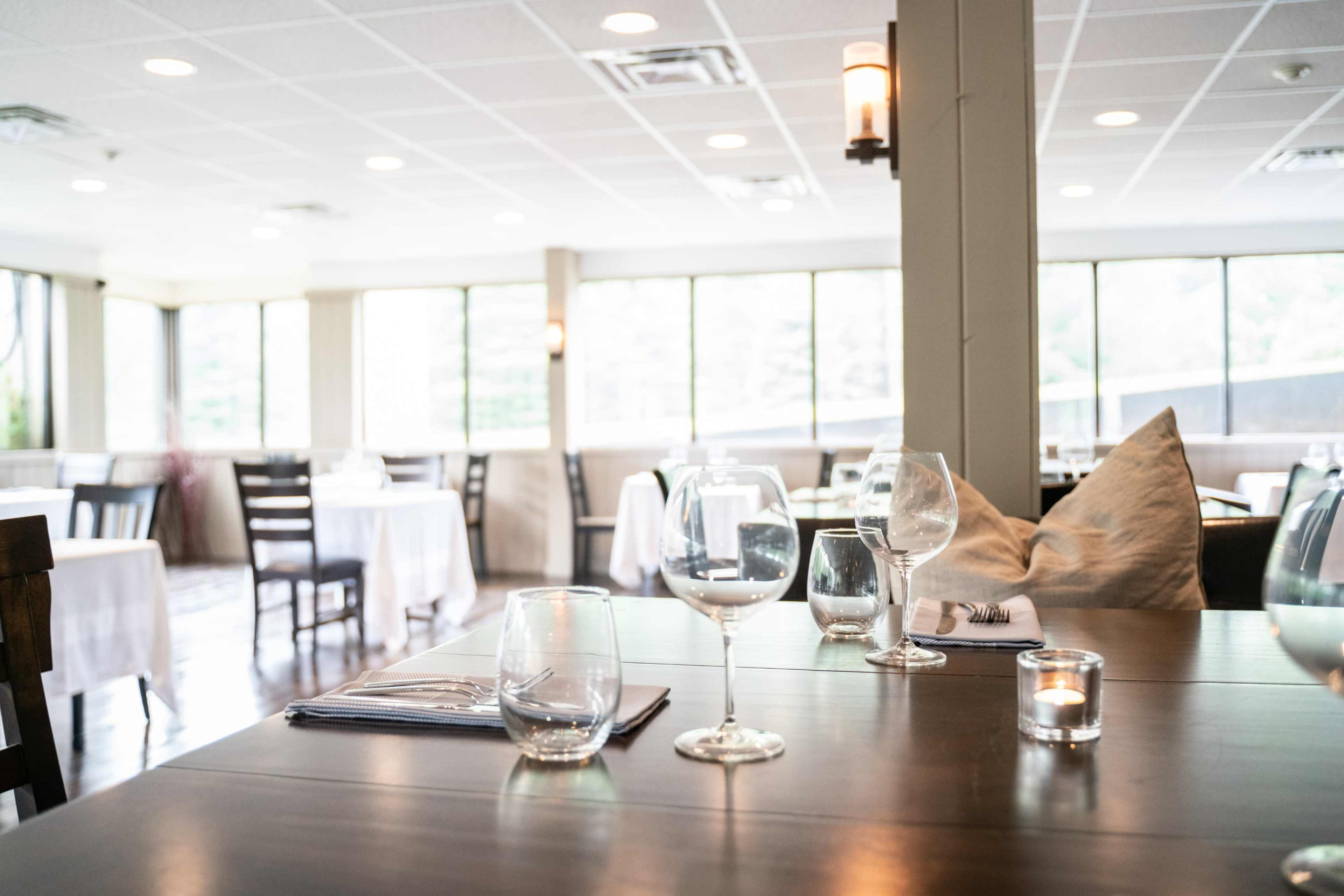 A well-lit restaurant interior with tables set for dining, featuring glassware and a candle on a wooden table.