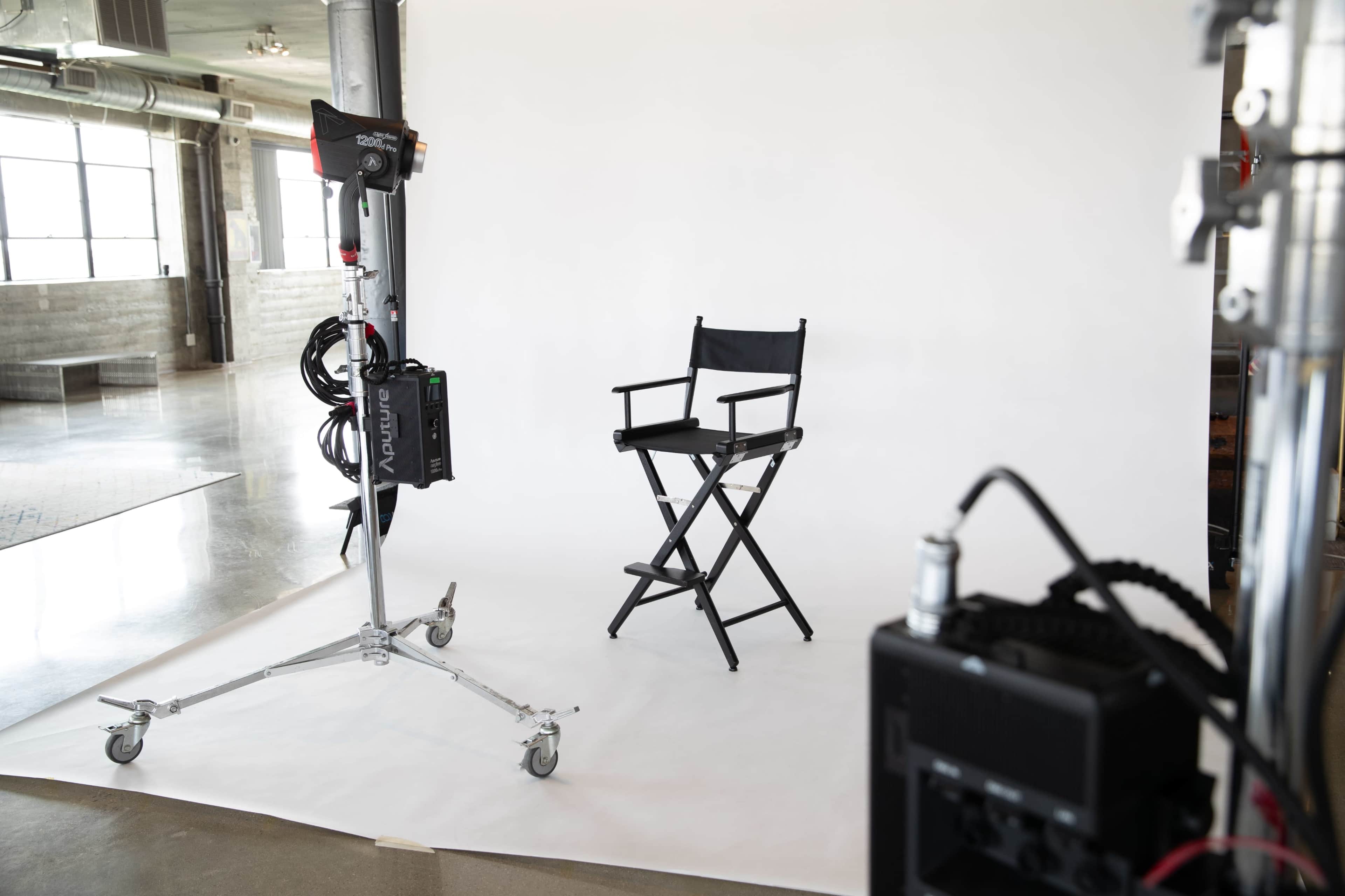 A black director's chair is positioned in front of a white backdrop in a photography studio.