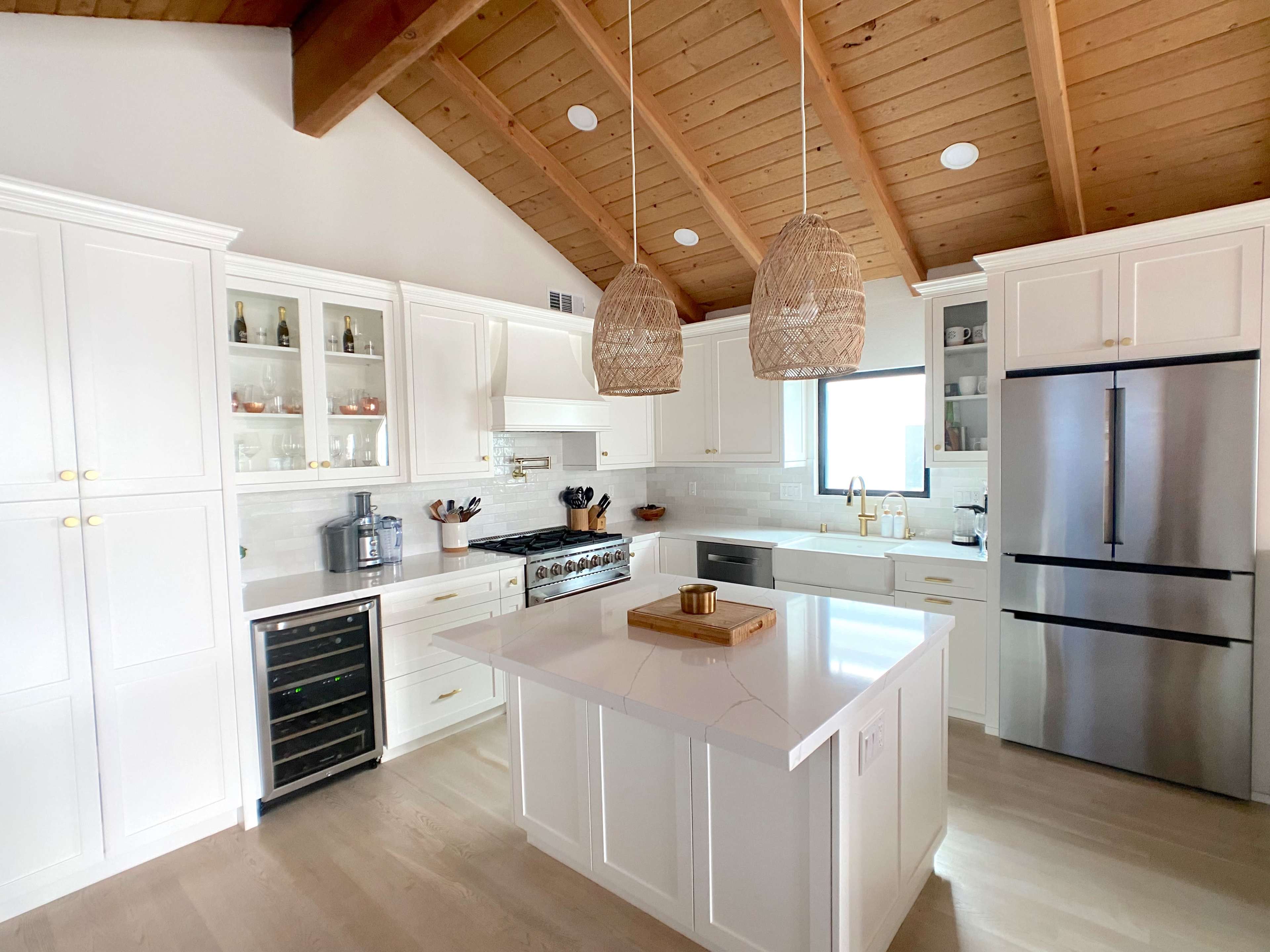 A modern kitchen with white cabinetry, a large island, stainless steel appliances, and wooden beams on the ceiling.