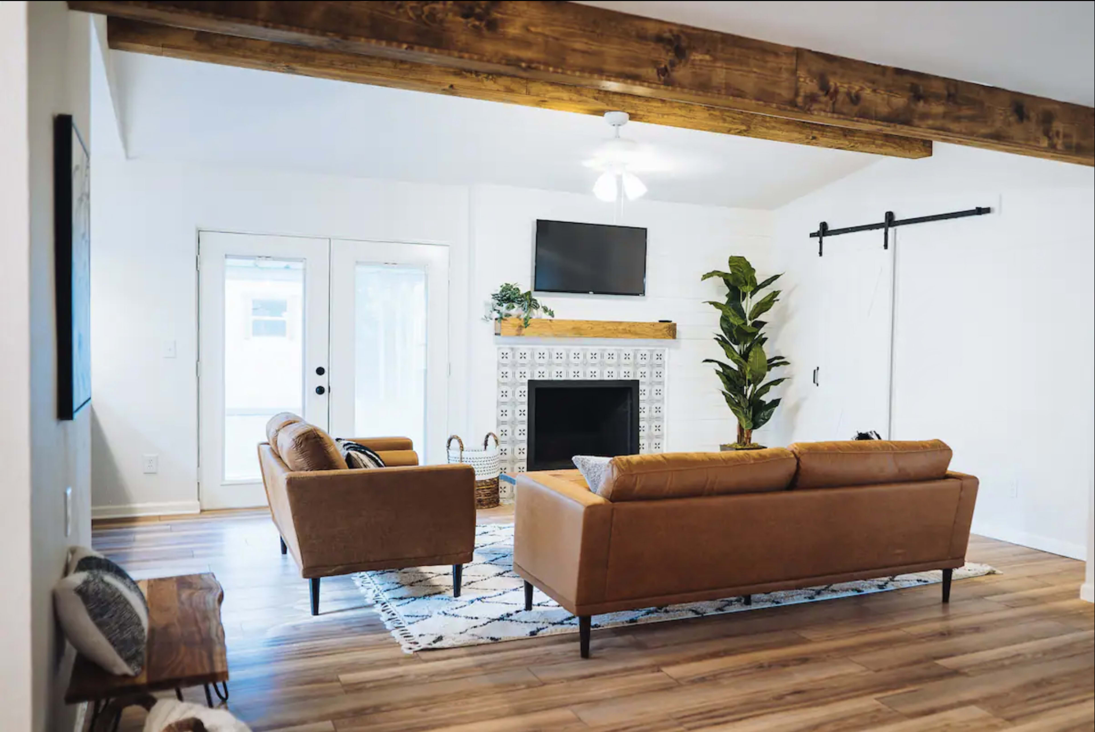 The living room features two leather sofas facing a decorative fireplace with a television mounted above it, and large sliding doors leading outside.