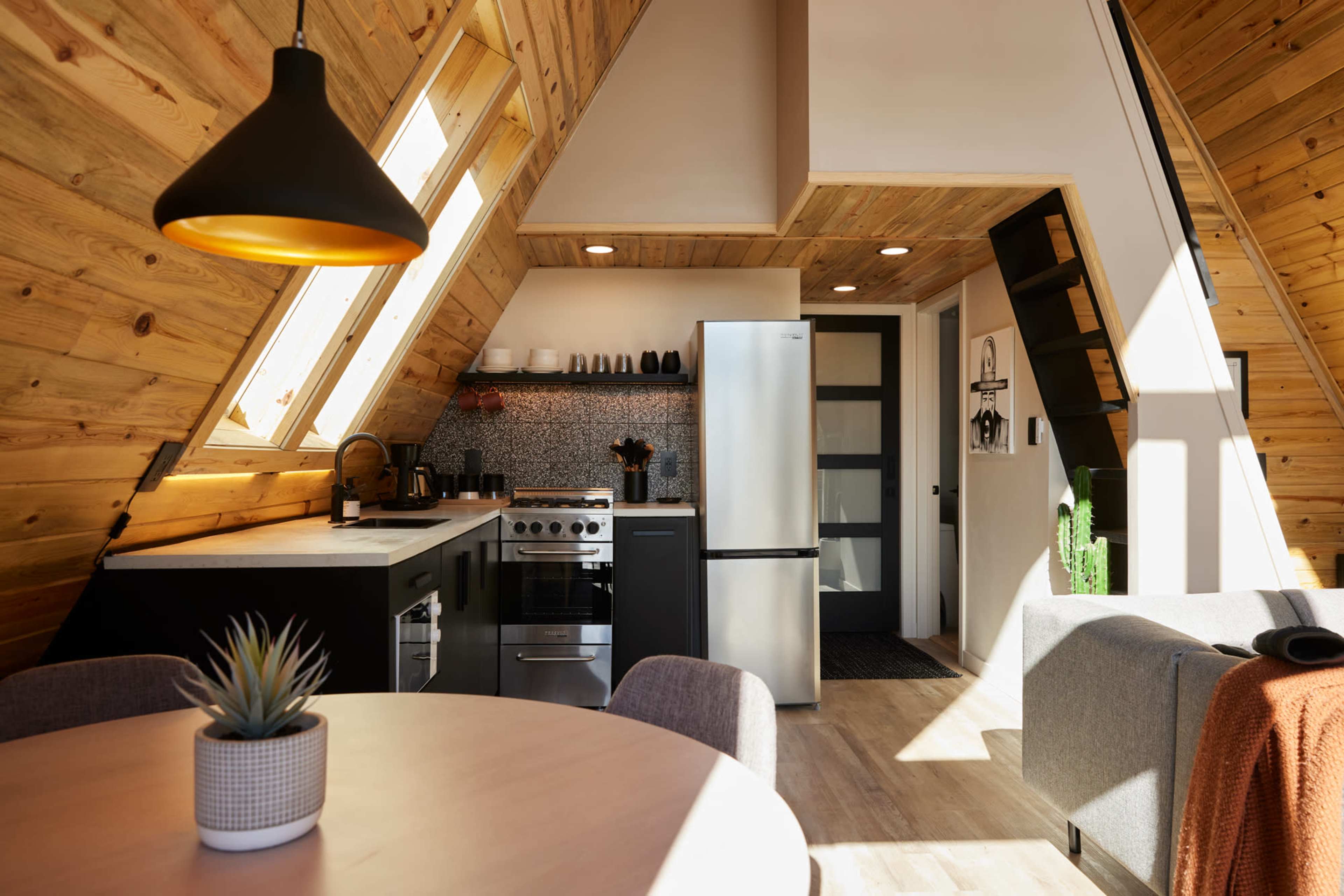 A modern kitchen with a triangular wooden ceiling features stainless steel appliances and a round dining table.