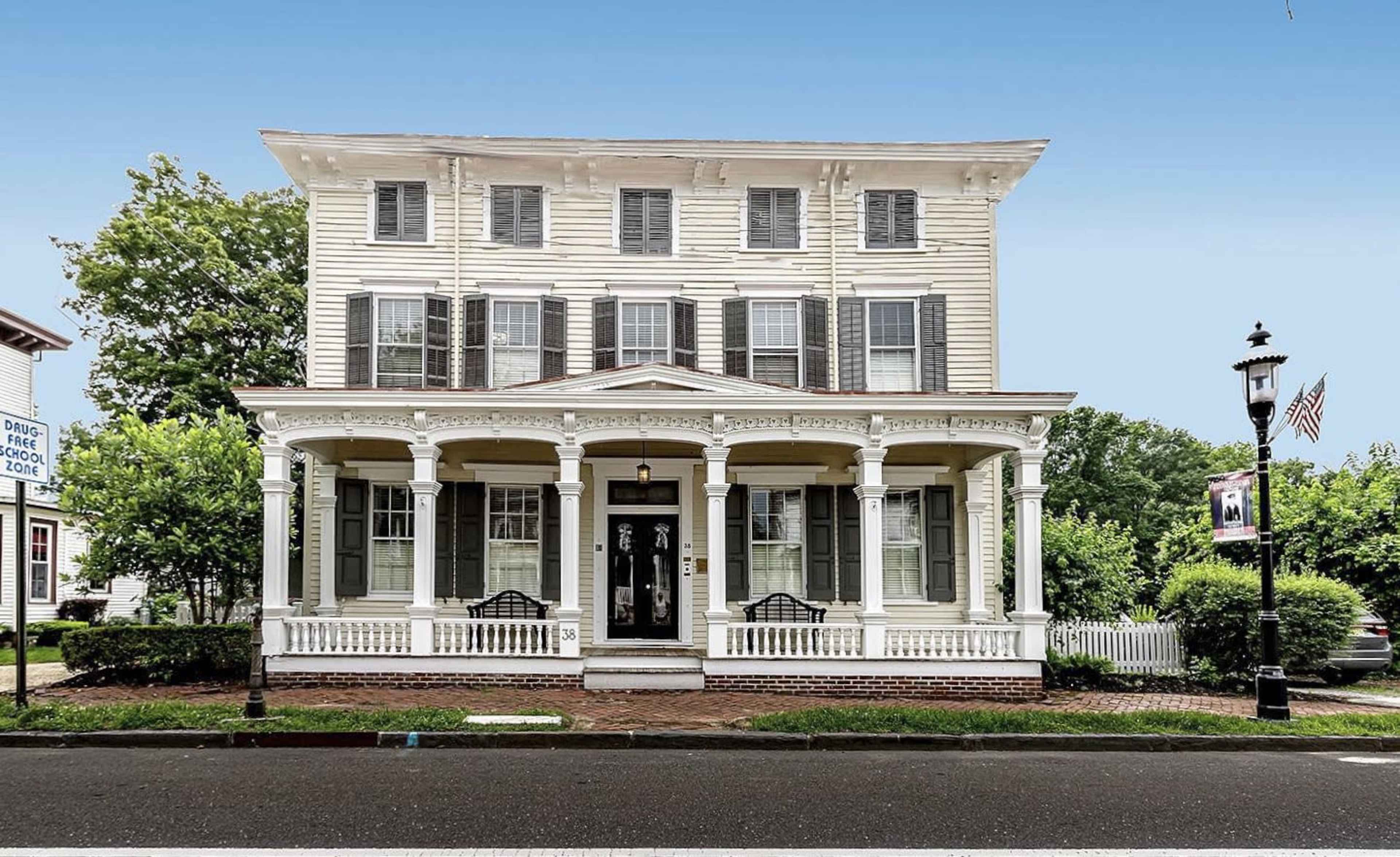 A three-story white house with a front porch supported by columns, featuring multiple windows with shutters.
