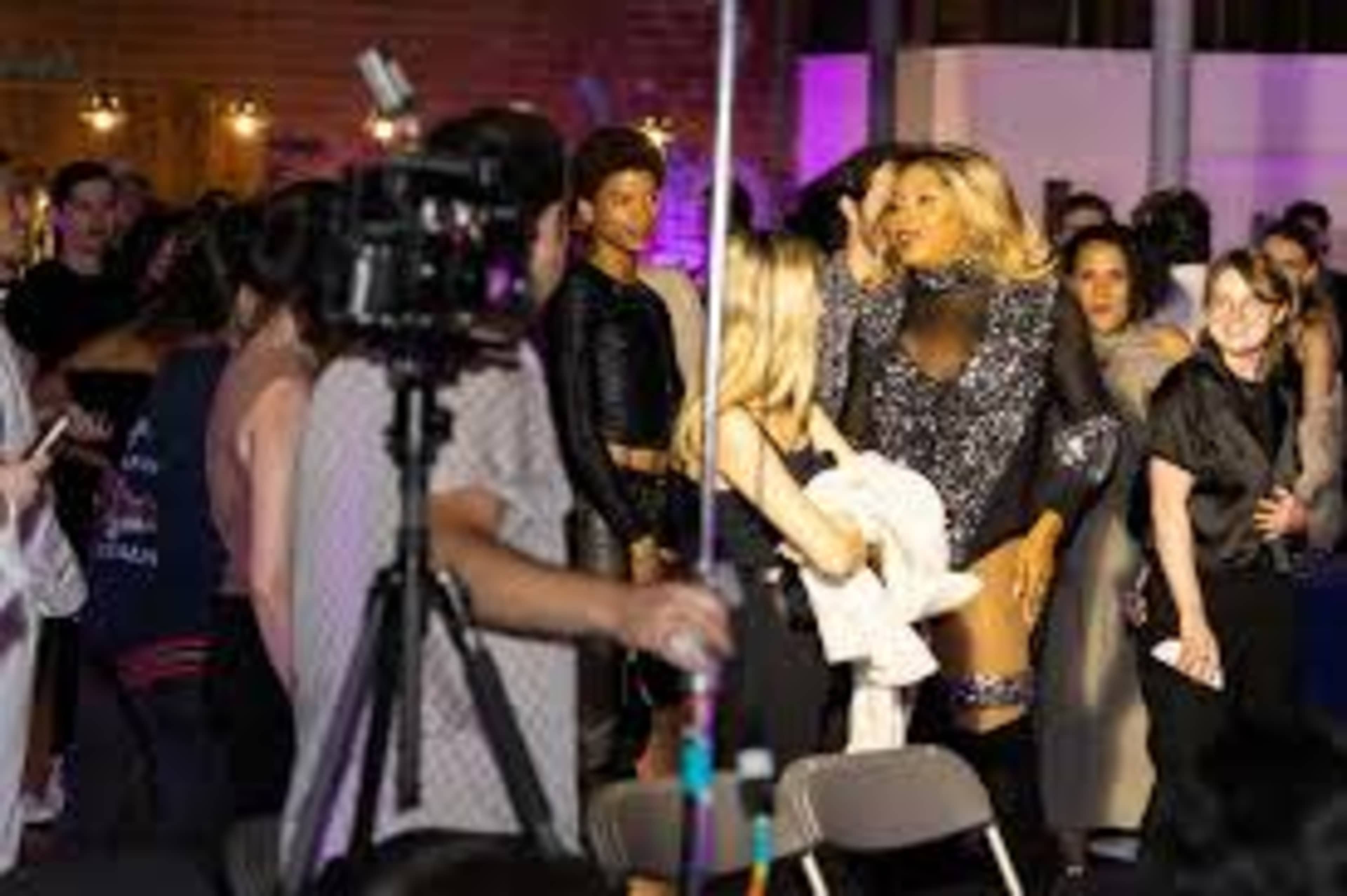 A group of people attends an event featuring a performer in a glamorous outfit, while cameras and lights are set up around them.