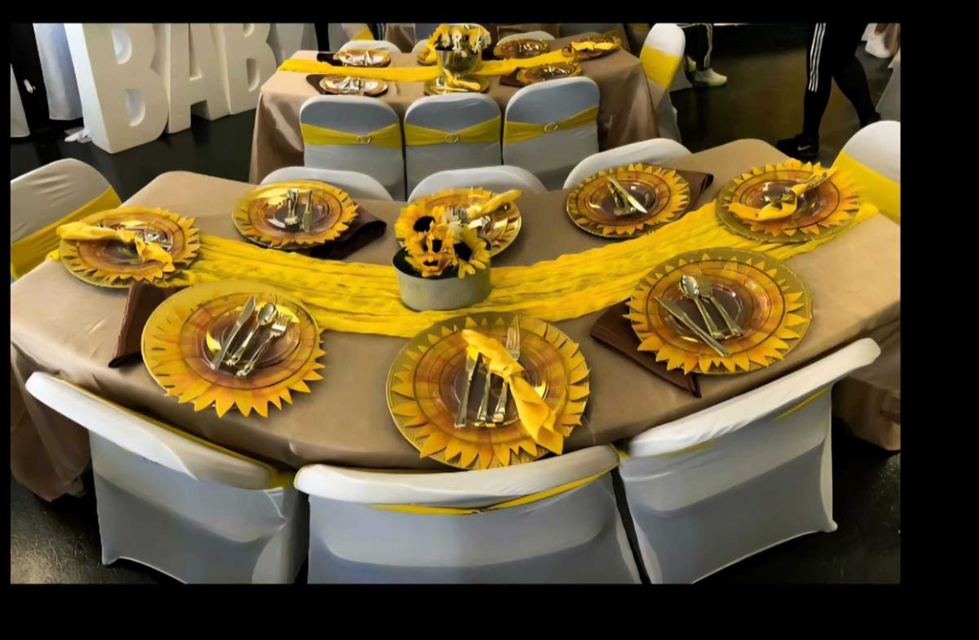 The image shows a decorated dining setup with multiple tables arranged in a circular layout, featuring sunflower-themed plates and yellow table runners.