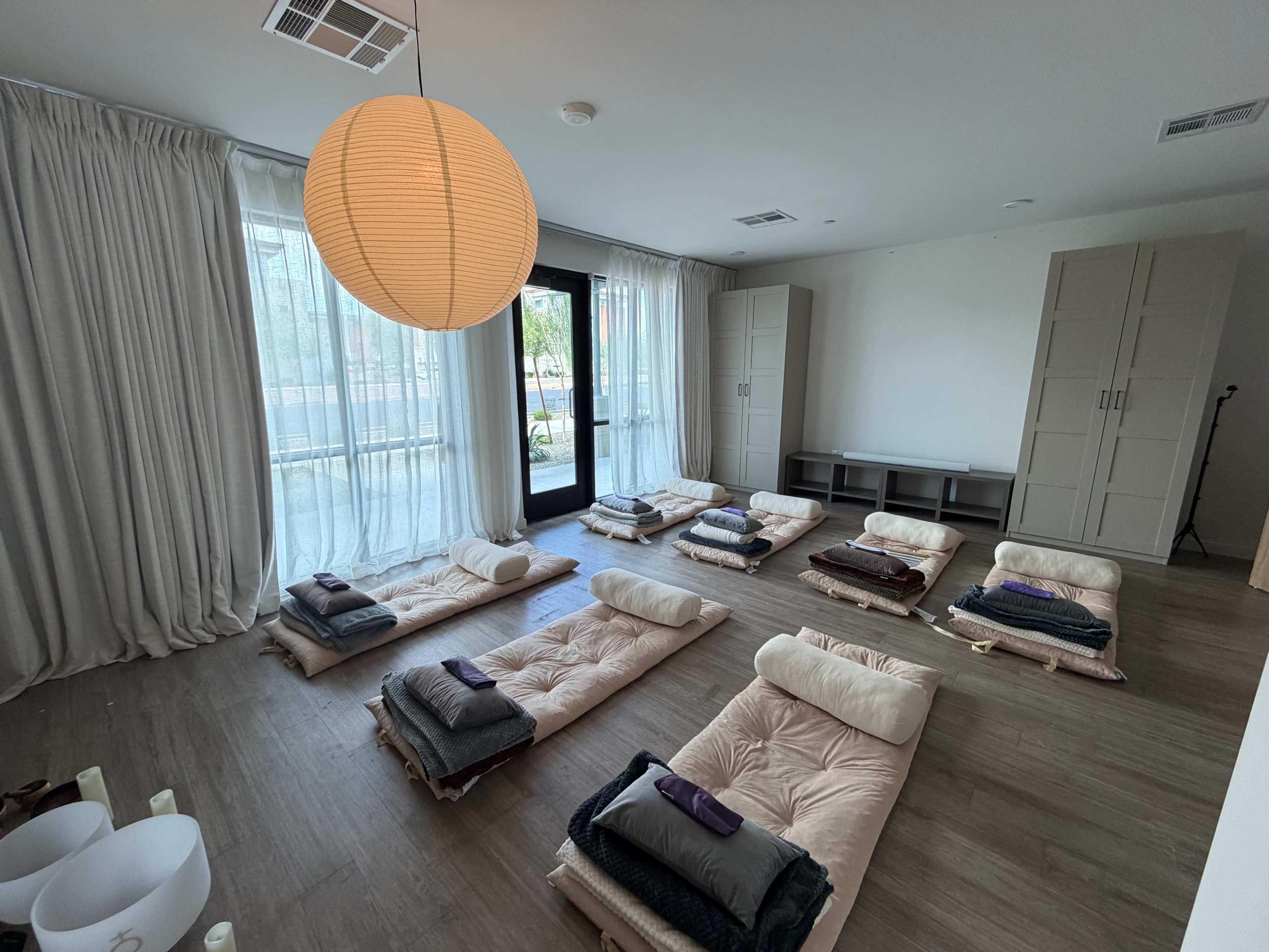 The room features several mats arranged neatly on the floor, with large windows and a pendant light hanging from the ceiling.